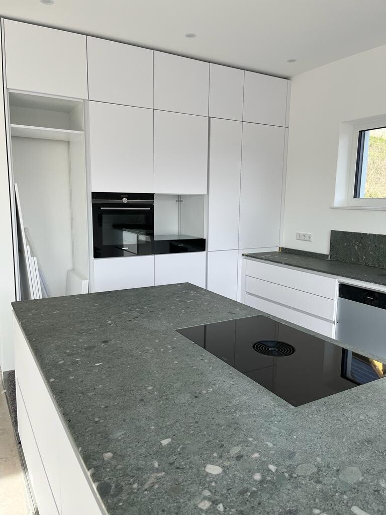 Moderne Küche mit weißen Schränken, grauer Granit-Arbeitsplatte und Induktionskochfeld auf der Insel.
