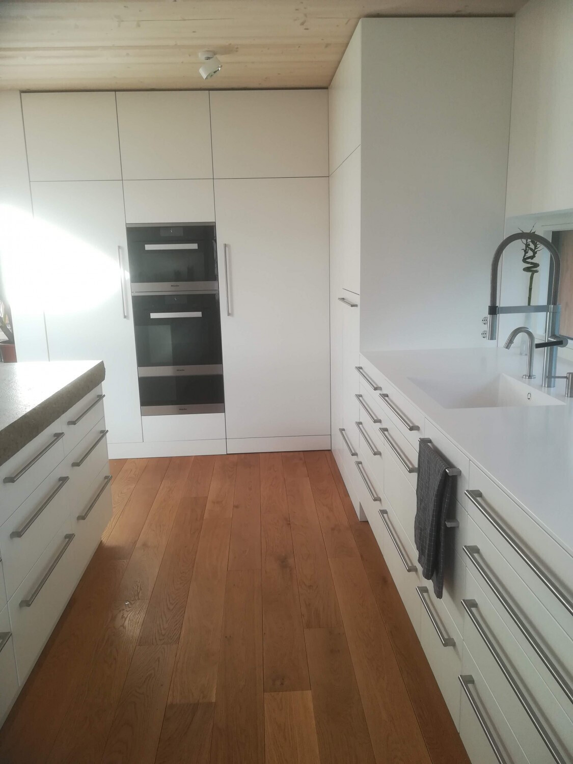 Moderne Küche mit weißen Fronten, Doppel-Backöfen, Spüle, Holzboden und Handtuch.