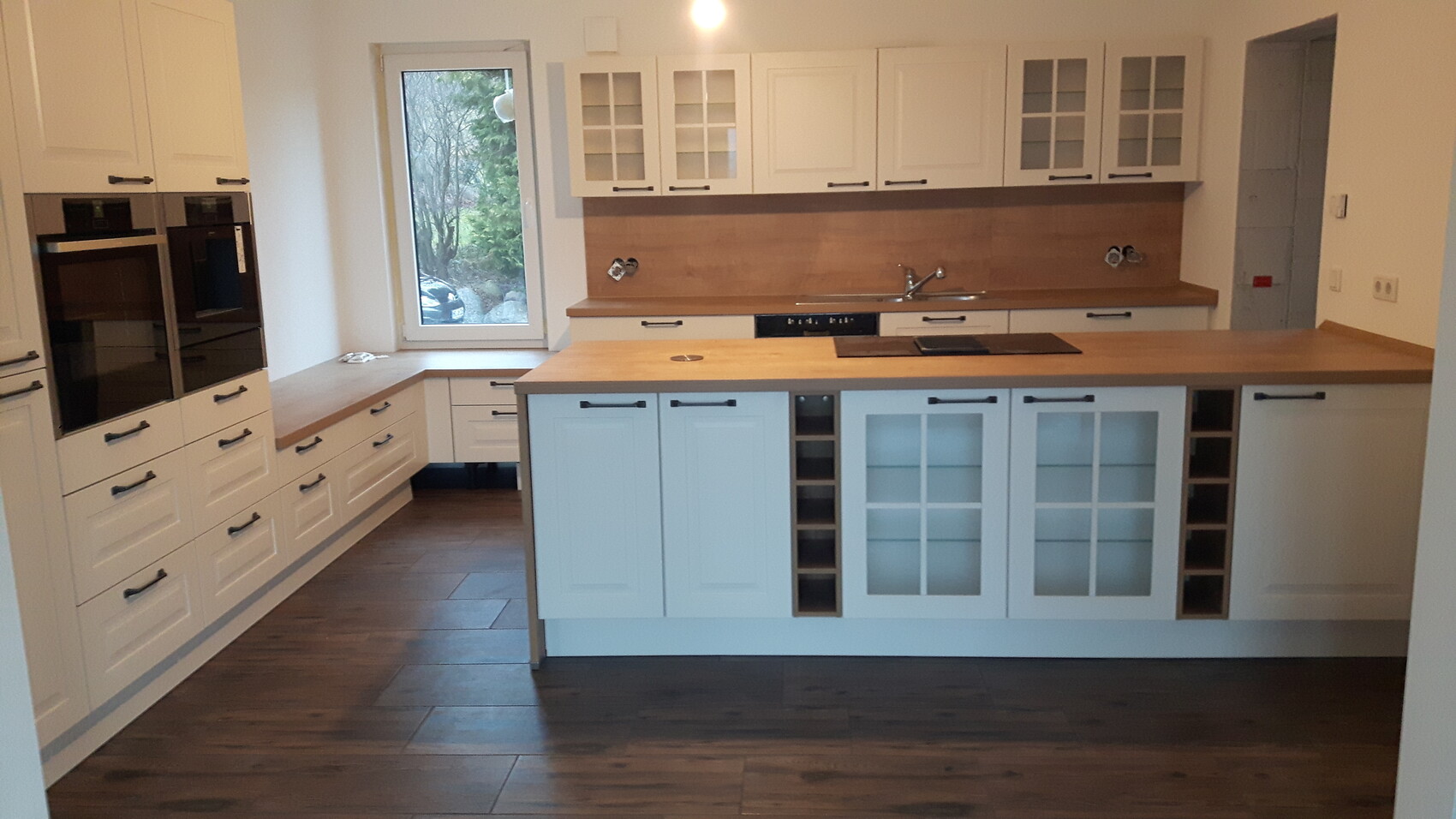 Moderne Küche mit weißen Schränken, Holz-Arbeitsplatten, Insel und Glasvitrine.
