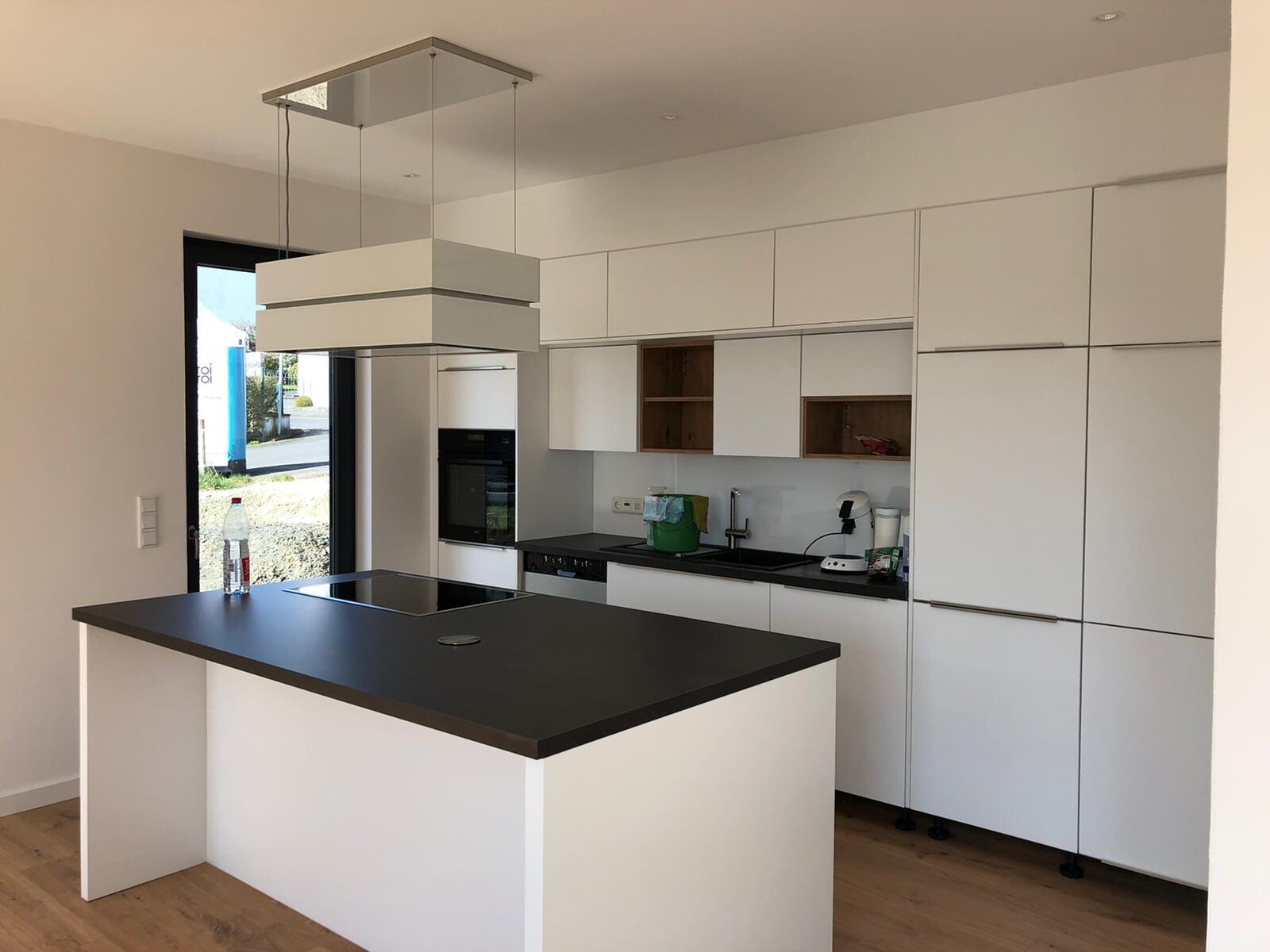 Moderne weiße Küche mit Insel, dunkler Arbeitsplatte, Spüle und Kaffeemaschine; Tür nach außen.