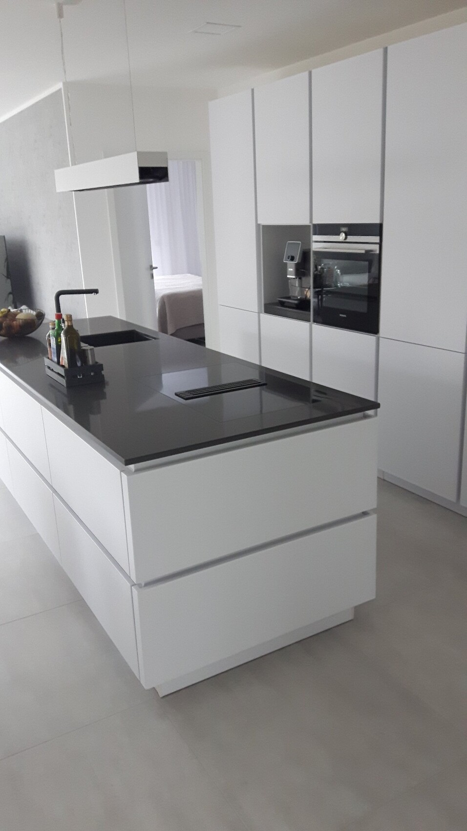 Moderne weiße Küche mit grauer Insel, Spüle, Armatur, Backofen und Kaffeemaschine.