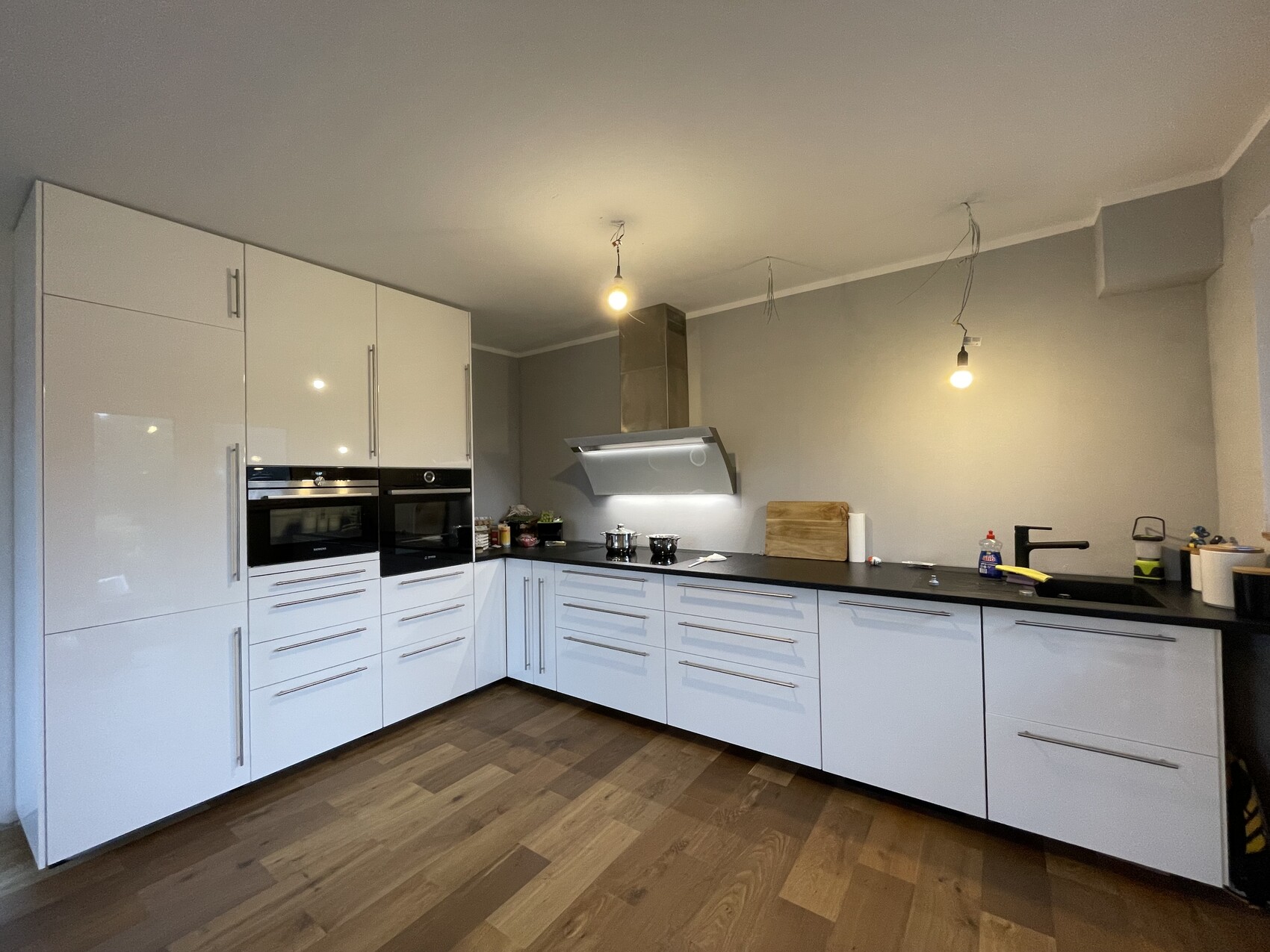 Moderne weiße Küchenzeile mit zwei Backöfen, Dunstabzug, Holzboden und Hängelampen.