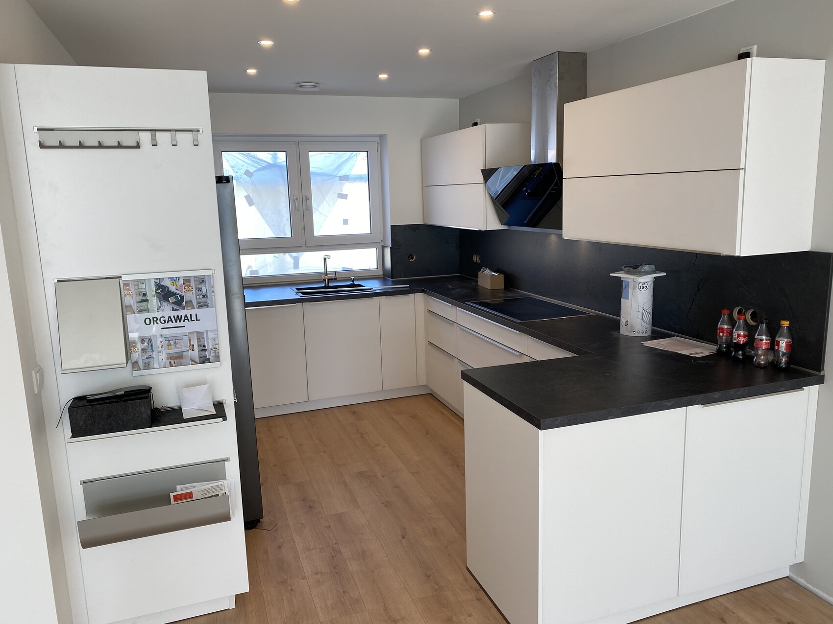 Moderne weiße Küche mit schwarzen Arbeitsplatten, Spüle unter Fenster, Kochfeld und Dunstabzug