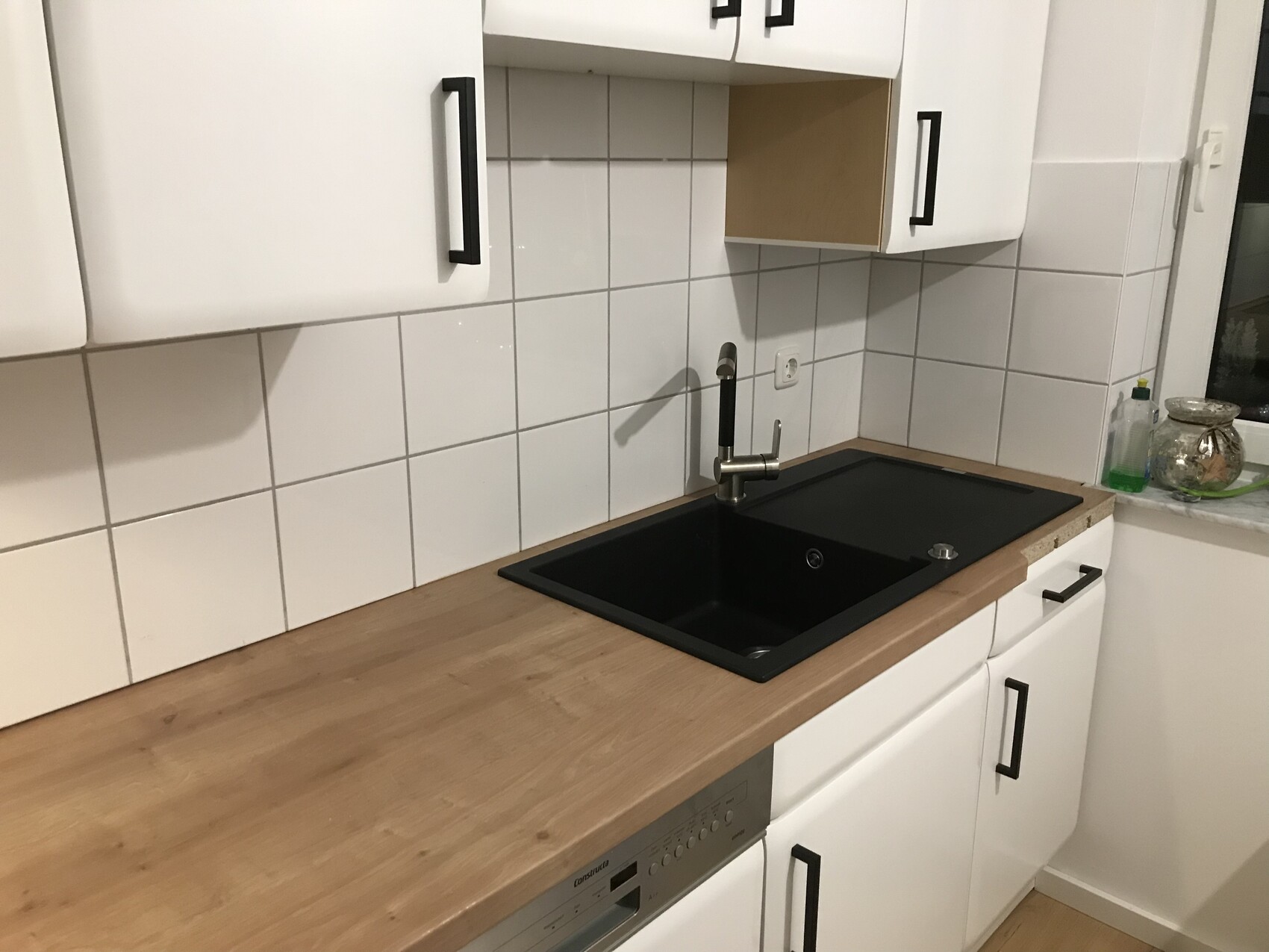 Küchenzeile mit schwarzer Spüle und Armatur, Holzarbeitsplatte, weiße Schränke und Fliesenwand