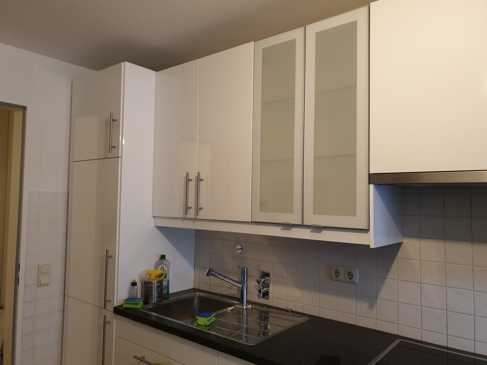 Moderne weiße Küche mit Spüle, Glasfronten an oberen Hängeschränken und Fliesenrückwand.