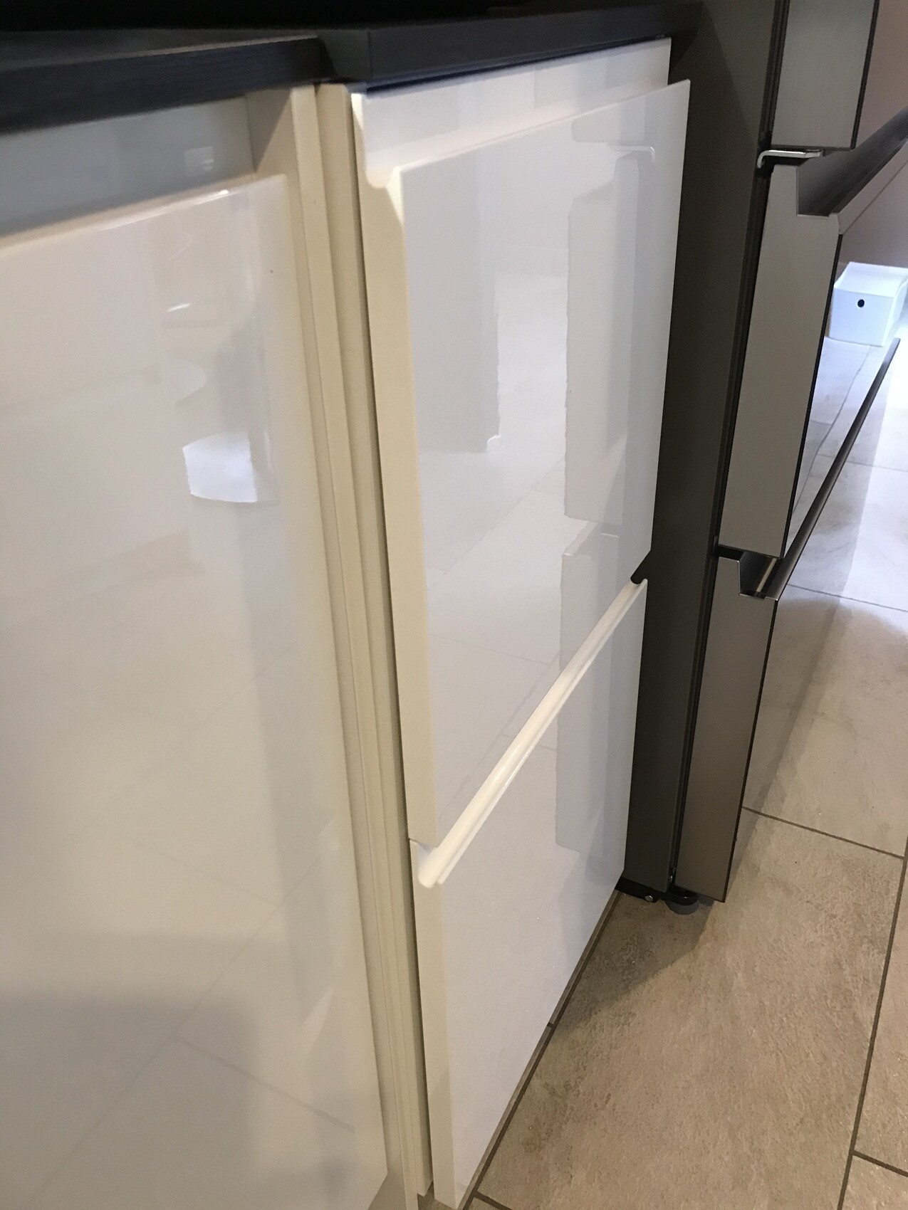 Weißer Unterbaukühlschrank mit Griff neben grauer Kücheneinrichtung auf Fliesenboden.