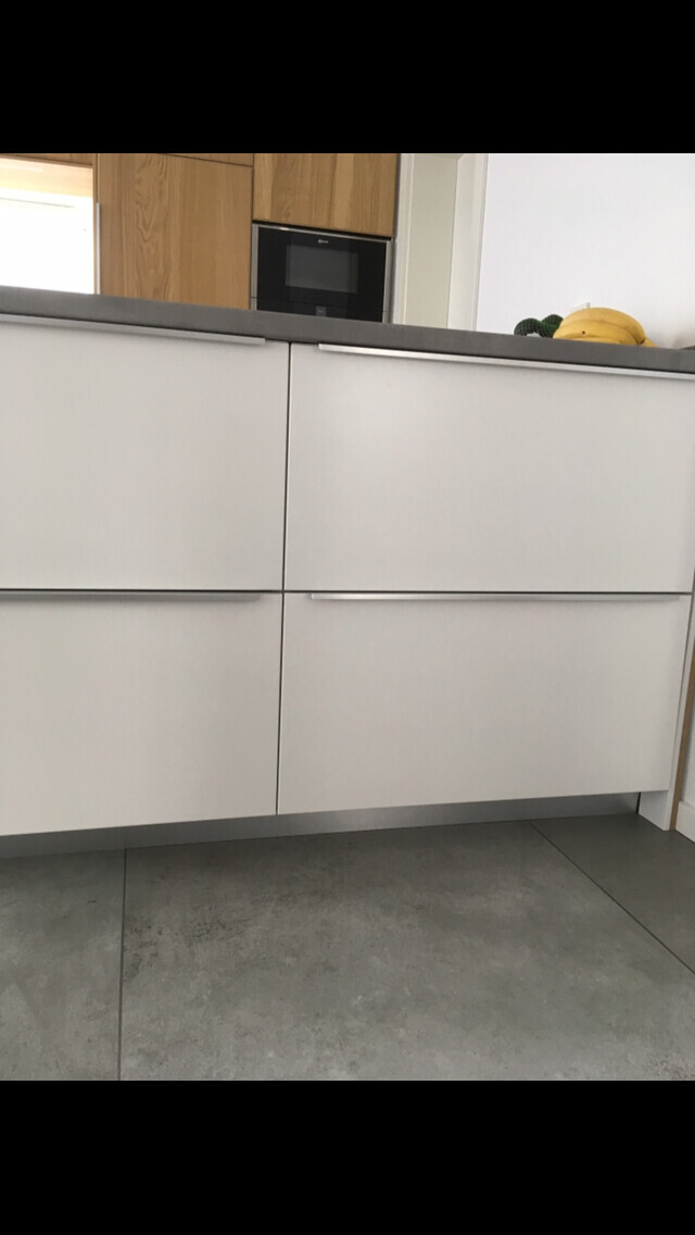 Moderne Küche: weiße Schubladen, graue Arbeitsplatte, Mikrowelle im Hintergrund, Banane auf der Fläche.
