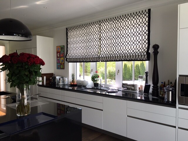 Moderne Küche mit weißen Schränken, schwarzer Arbeitsplatte, Rosen auf Insel, Fenster-Rollo.