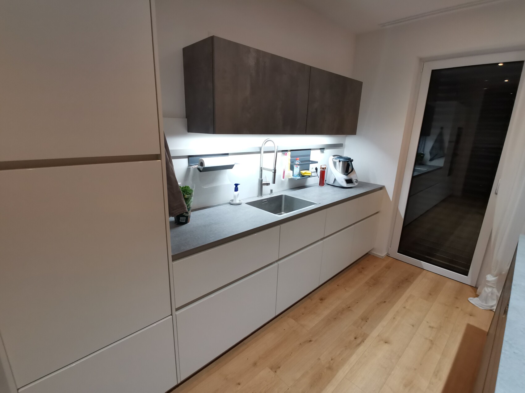 Moderne Küche: weiße Unterschränke, dunkle Oberschränke, Spüle, Küchenmaschine am Fenster/Glas-Tür