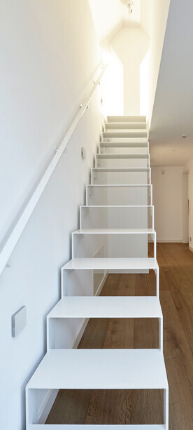 Moderne weiße Treppe mit offenen Stufen in hellem Innenraum, Handlauf an der Wand.