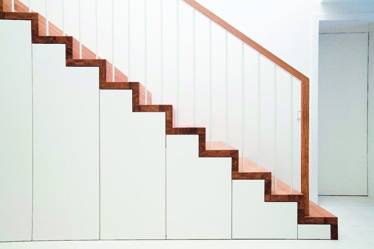 Moderne Innentreppe mit weißen Stufen, Holzkante und Glasgeländer in hellem Raum