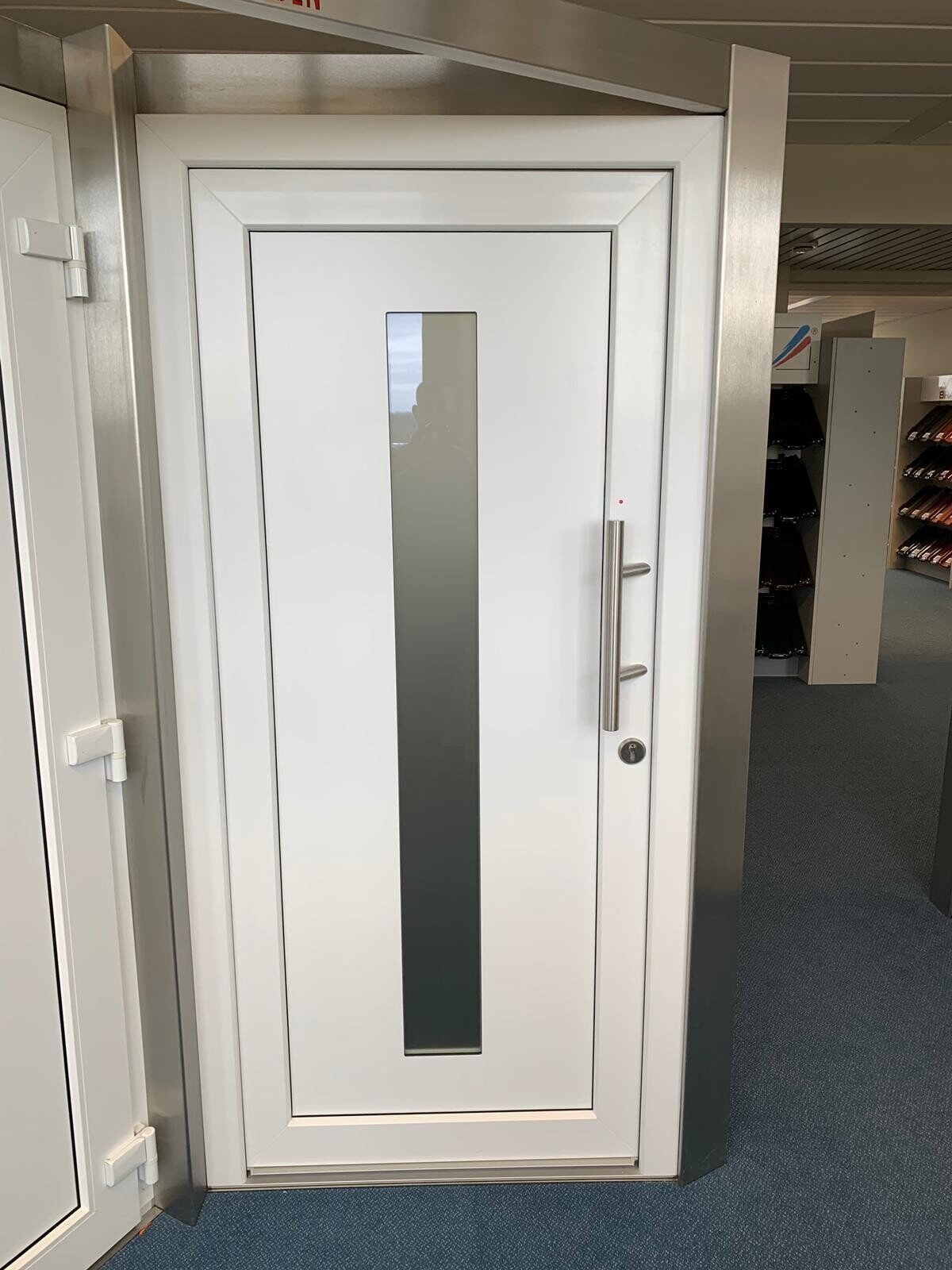 Weiße Tür mit vertikalem Glasfenster und langem Metallgriff in einem Raum.