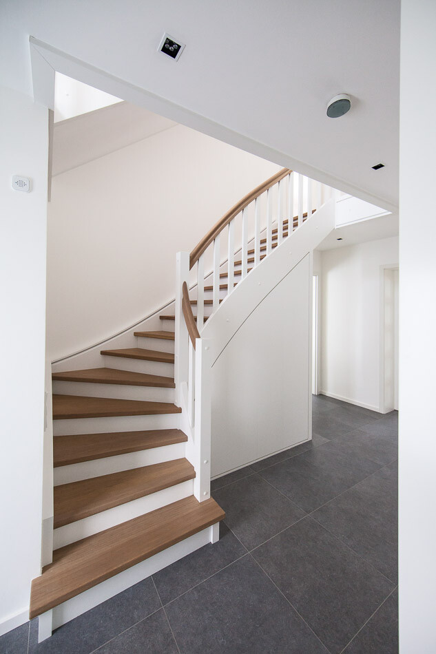 Moderne Innentreppe mit Holzstufen, weißem Geländer und grauem Fliesenboden.