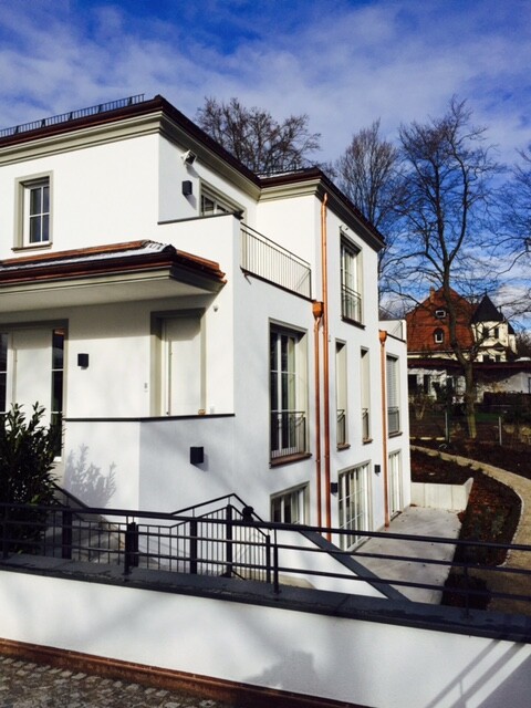 Weißes modernes Wohnhaus mit Balkonen, Treppe und blauem Himmel.