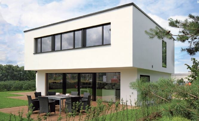 Moderner zweistöckiger, weißer Neubau mit großen Fenstern, Terrasse und Gartenmöbeln.