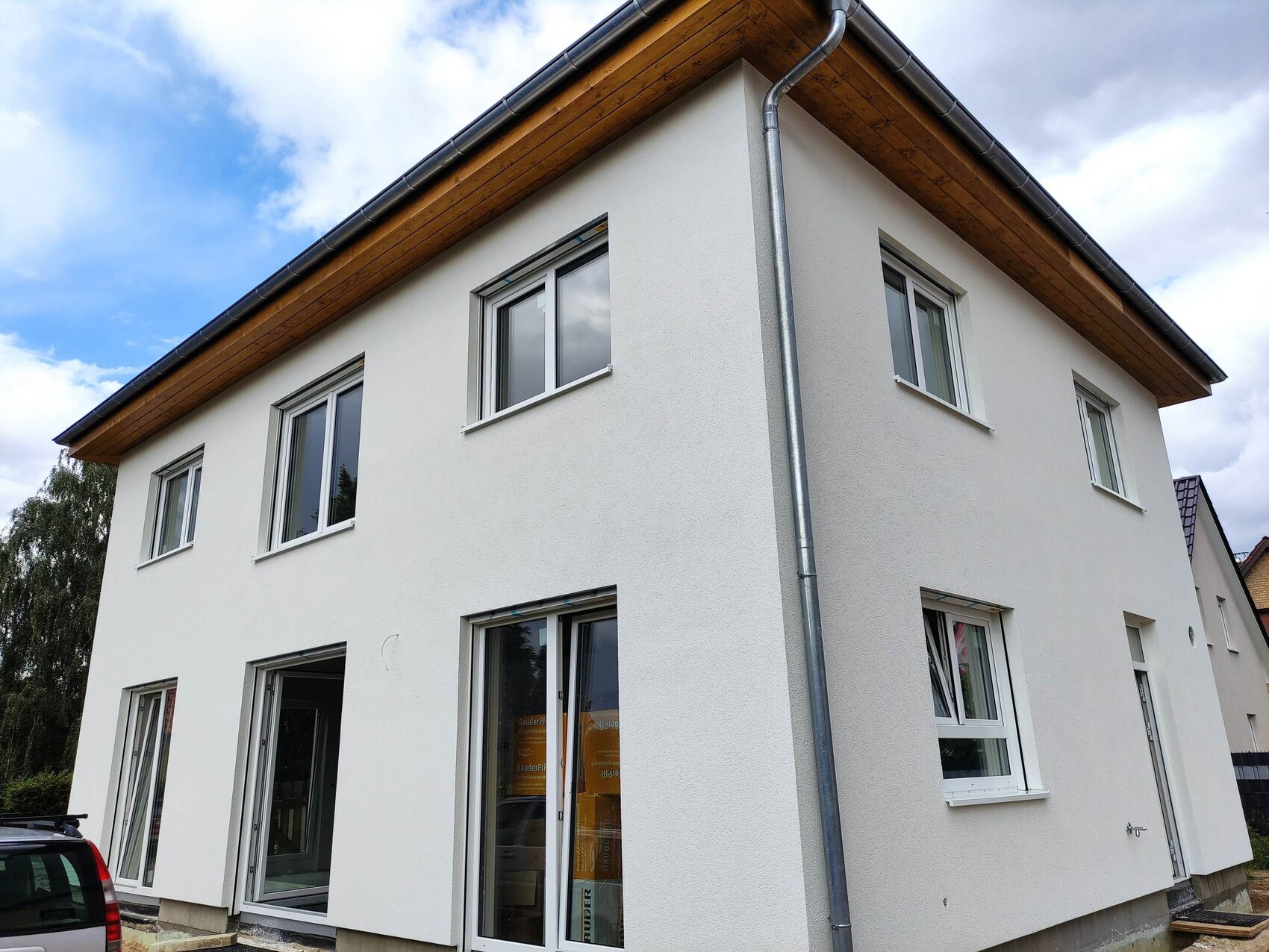 Modernes zweigeschossiges Einfamilienhaus mit weißer Putzfassade, Holzdachüberstand und Regenrinne.