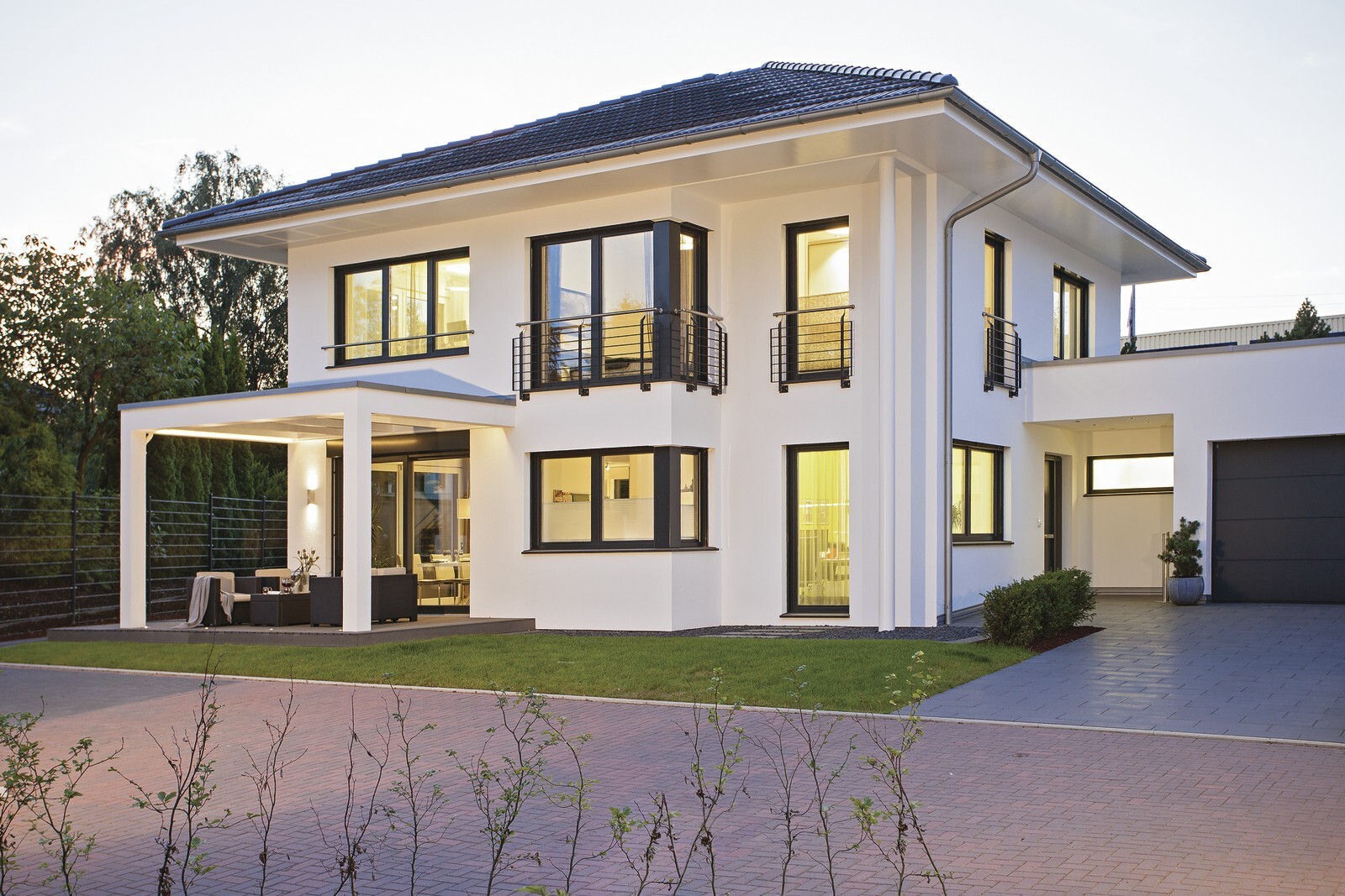 Modernes weißes Einfamilienhaus mit großen Fenstern, Balkon, Terrasse mit Sitzgruppe und Garage.