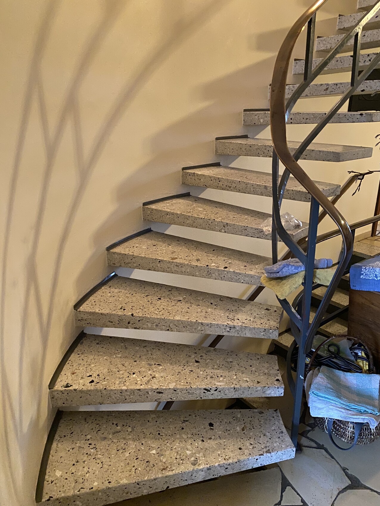 Kurvige Treppe mit terrazzo-Stufen und schwarzem Metallgeländer; Reinigungsutensilien rechts.
