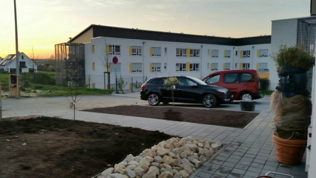 Parkplatz vor Wohnanlage mit zwei Autos, Gehwegplatten und Abendsonne.