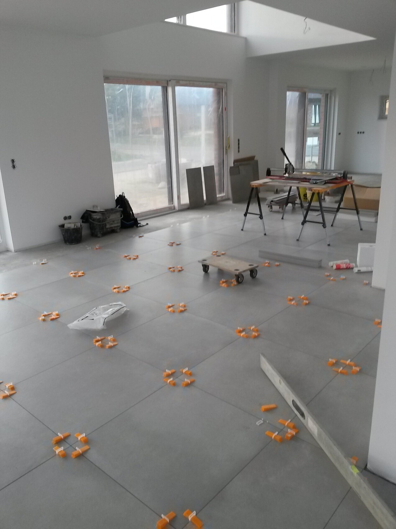 Heller Innenraum im Bau mit Fliesenboden, verstreuten orange Fliesenabstandhaltern und Werkbank.