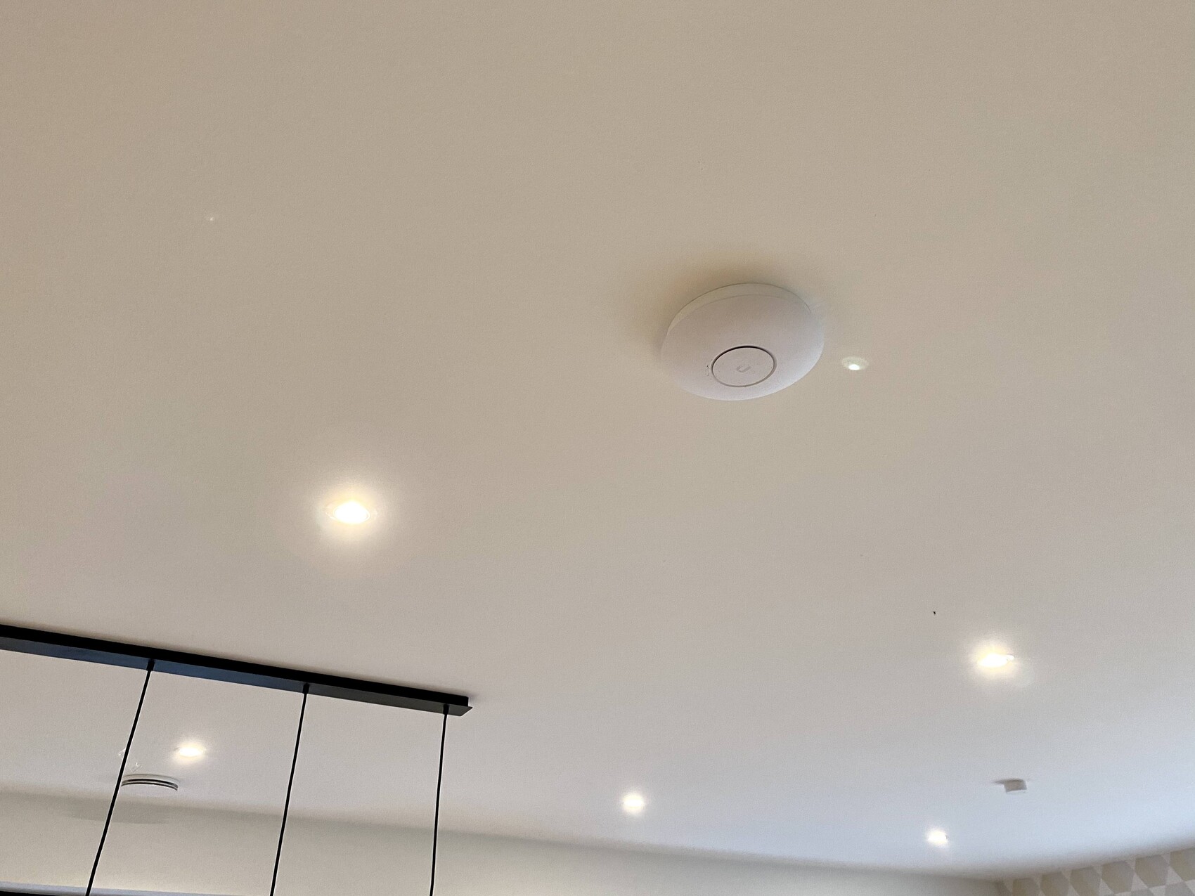 Weiße Decke mit mehreren Downlights; zentrales rundes Rauchmeldergerät, links Pendelleiste.