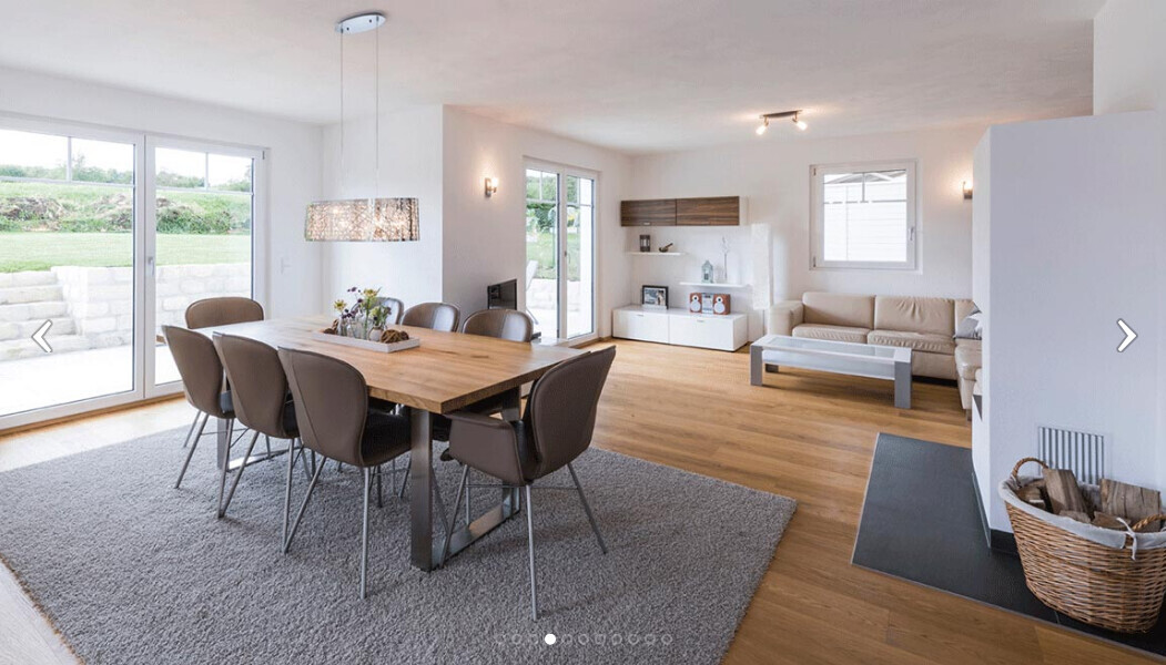 Offener Wohn- und Essraum mit Holztisch, braunen Stühlen, Sofa, Kamin und Glasfronten.