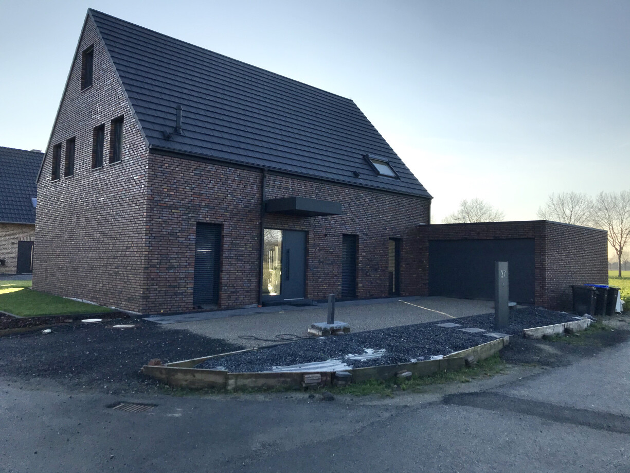 Zweistöckiges Backsteinhaus mit dunklem Ziegeldach, Glastür und Garage.