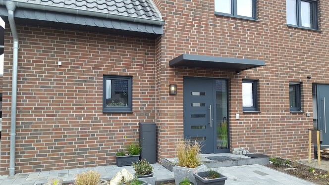 Moderne Backsteinfassade eines Wohnhauses mit einer dunkelblauen Tür, Fenstern und Pflanzkübeln.