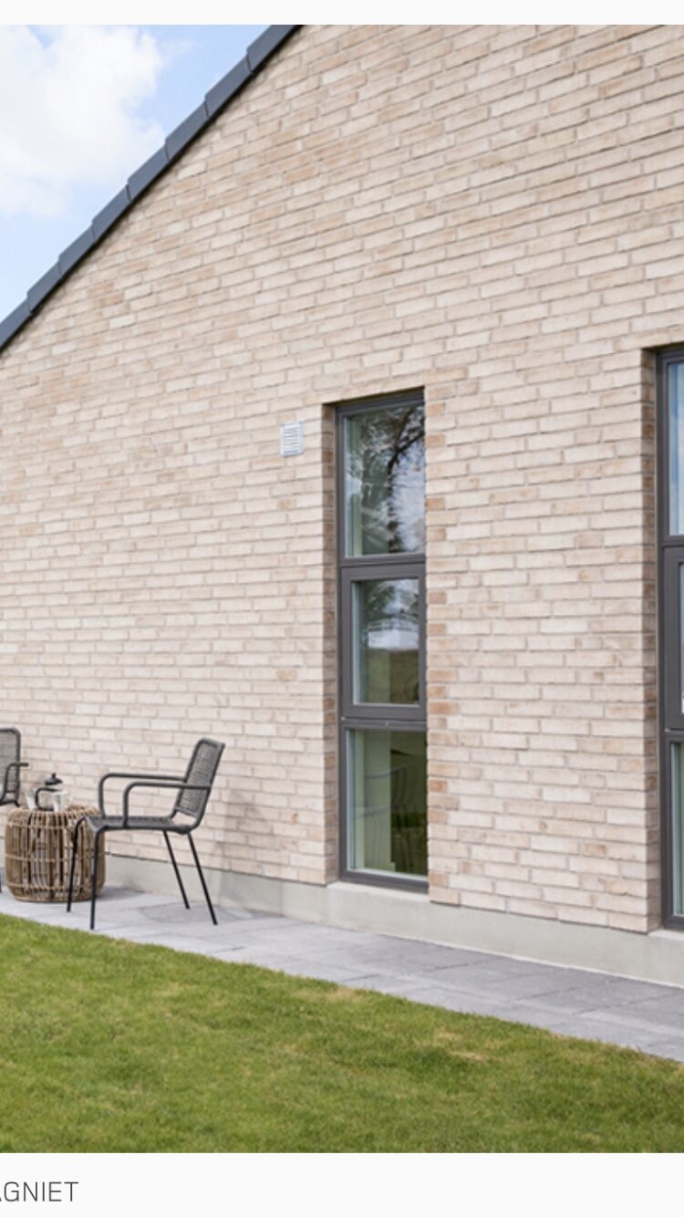 Außenansicht eines Backsteinhauses mit Terrasse, zwei Stühlen und kleinem Korbtisch.