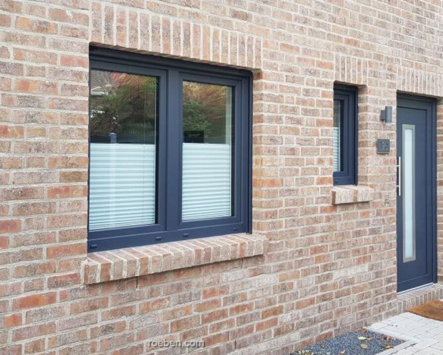 Außenseite eines Ziegelhauses mit dunkelblauen Fensterrahmen, zwei Fenster und Tür mit Glasfüllung.