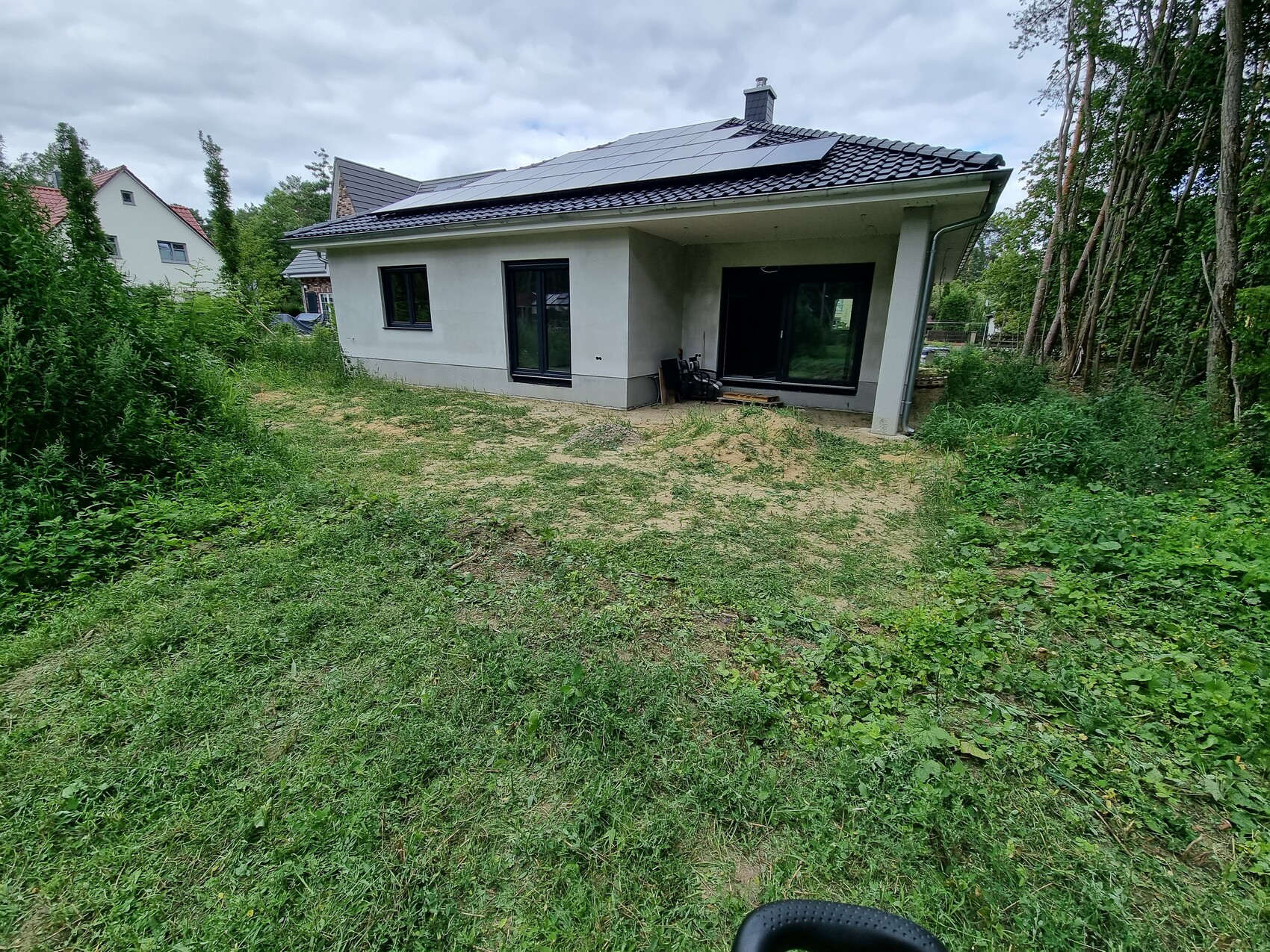 Modernes Einfamilienhaus von außen mit Solarpanelen auf dem Dach und grünem Garten.