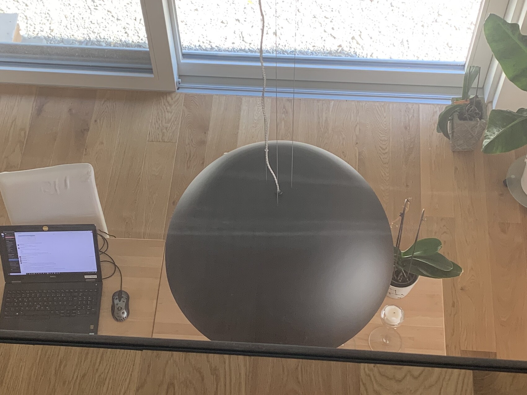 Von oben: Laptop auf Holztisch, großer schwarzer runder Lampenschirm, Pflanzen und Kerze.
