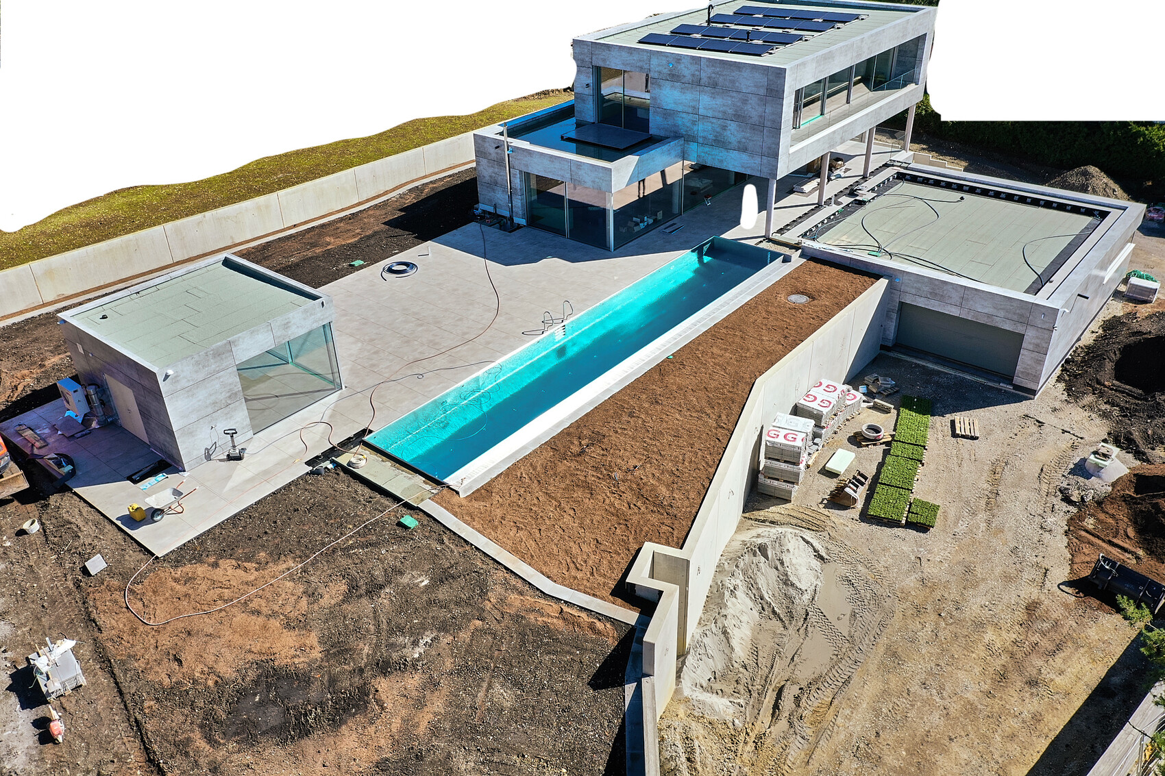 Luftaufnahme eines modernen Hauses im Bau mit langem Außenpool, Solaranlagen auf dem Dach.