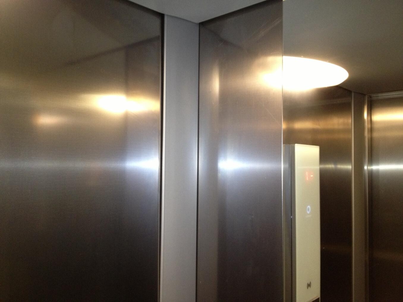 Innenraum eines Aufzugs mit Edelstahlwänden, beleuchtet und reflektierenden Oberflächen