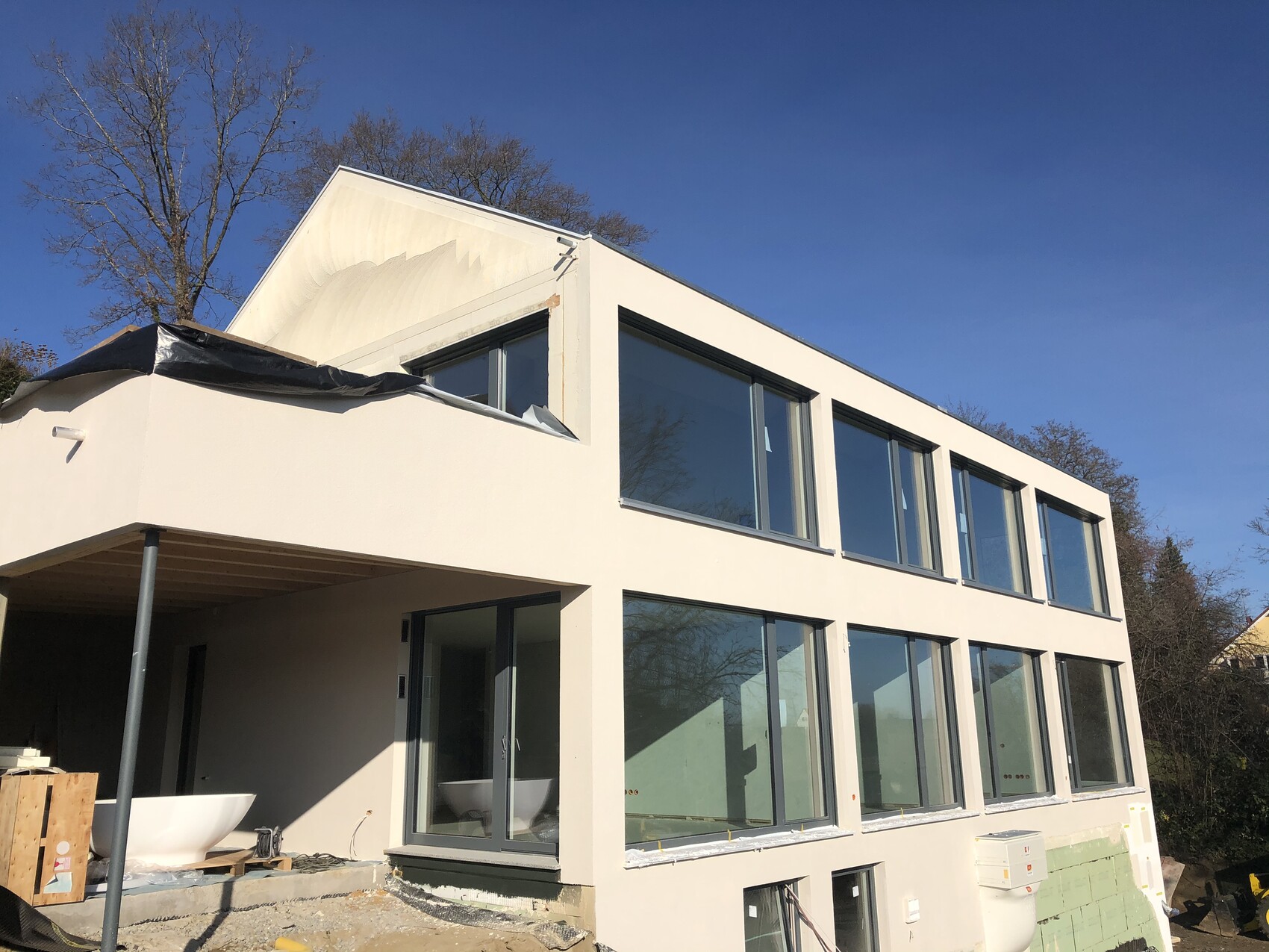 Modernes weißes Haus mit großen Fenstern, Bauarbeiten im Außenbereich und Baumaterialien.