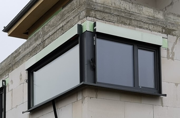 Schwarz gerahmtes Erkerfenster in einer Rohbauwand eines Neubaus.