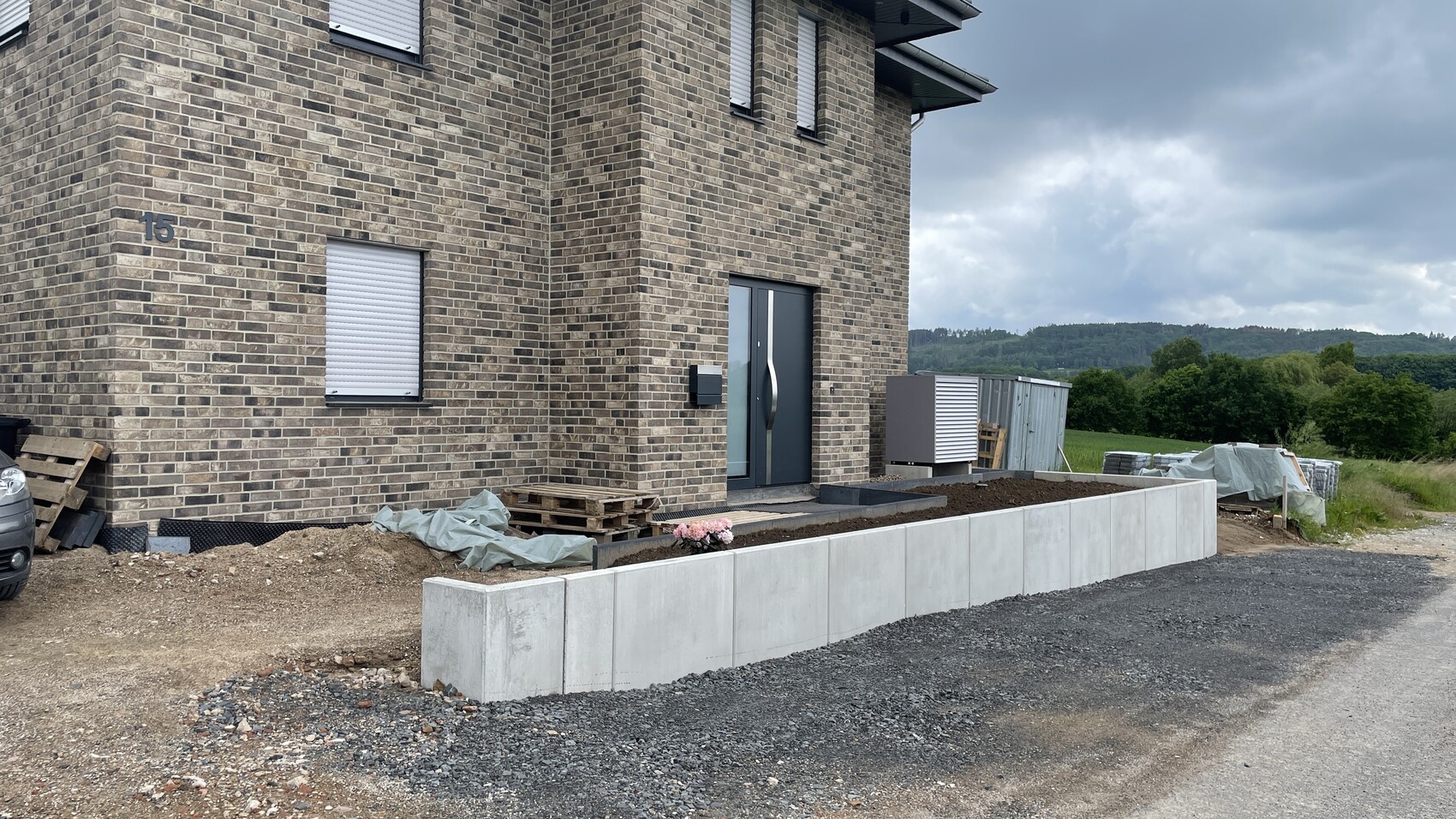Mehrfamilienhaus aus braunen Ziegeln mit Eingangstür; Bauarbeiten, Paletten, Betonmauer.