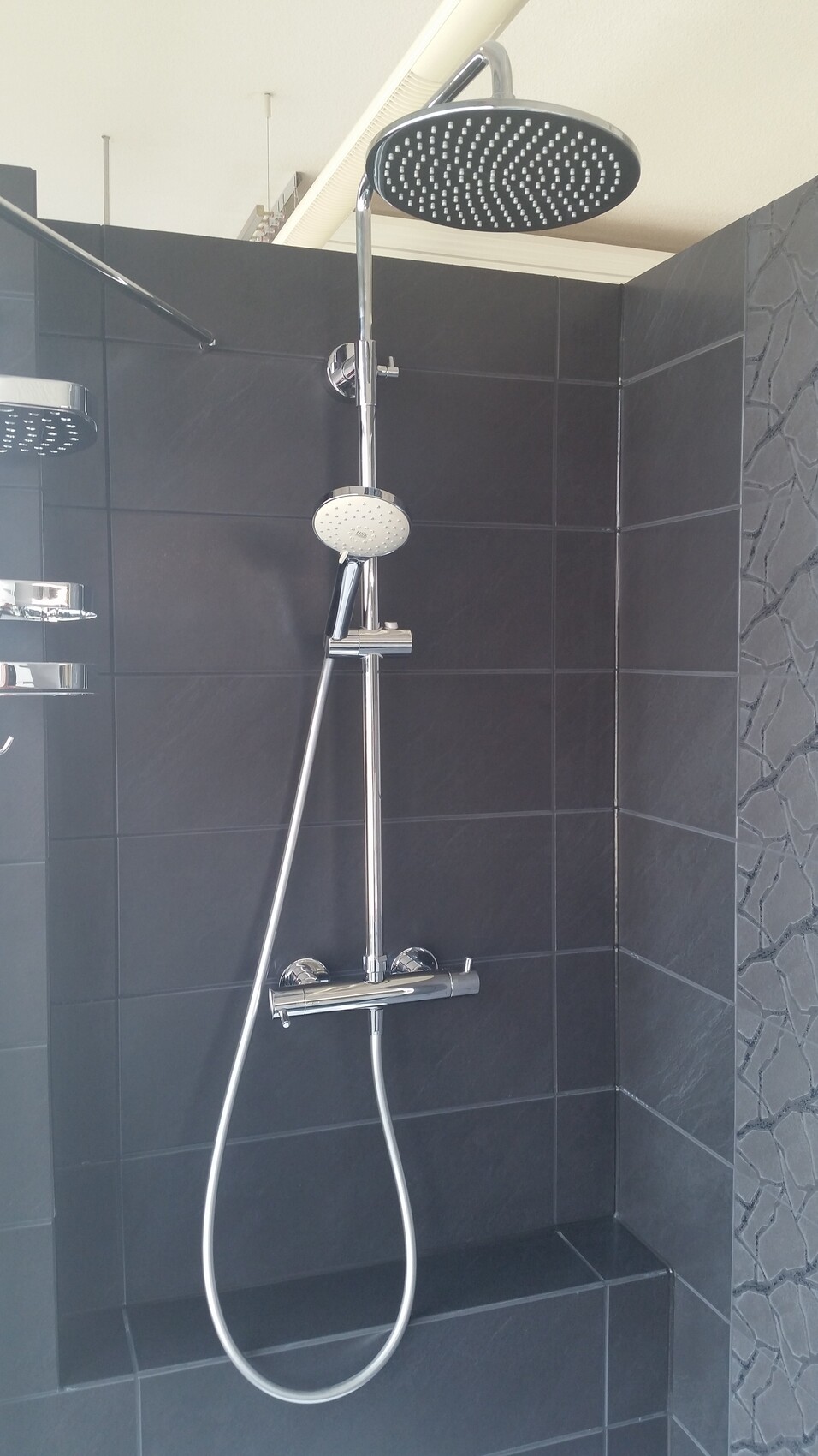 Moderner Duschbereich mit großer Decken-Dusche, Handbrause und dunklen Fliesen.
