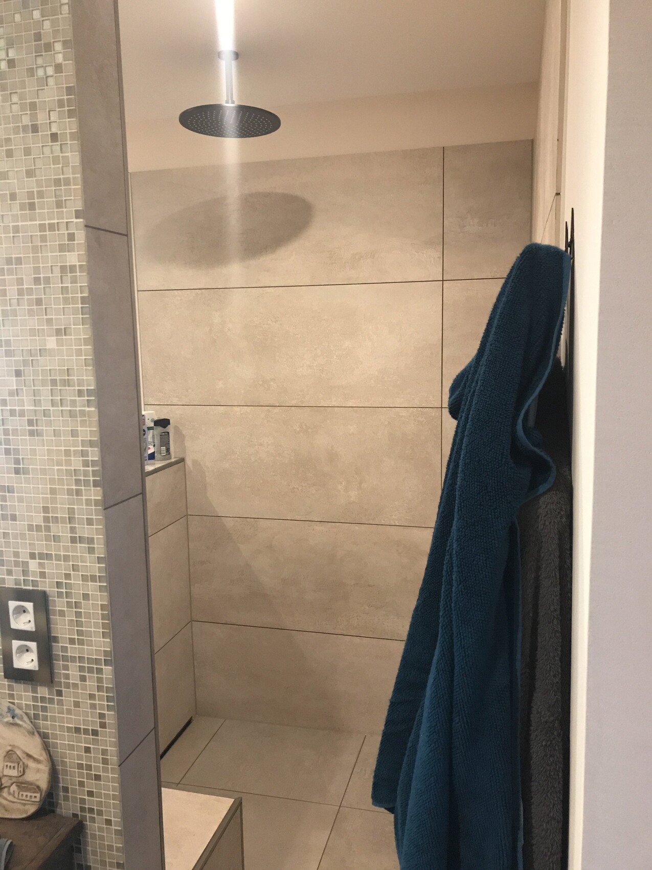 Offene Dusche mit großem Regen-Duschkopf, beige Fliesen, linke Mosaikfliesen, blaues Handtuch.