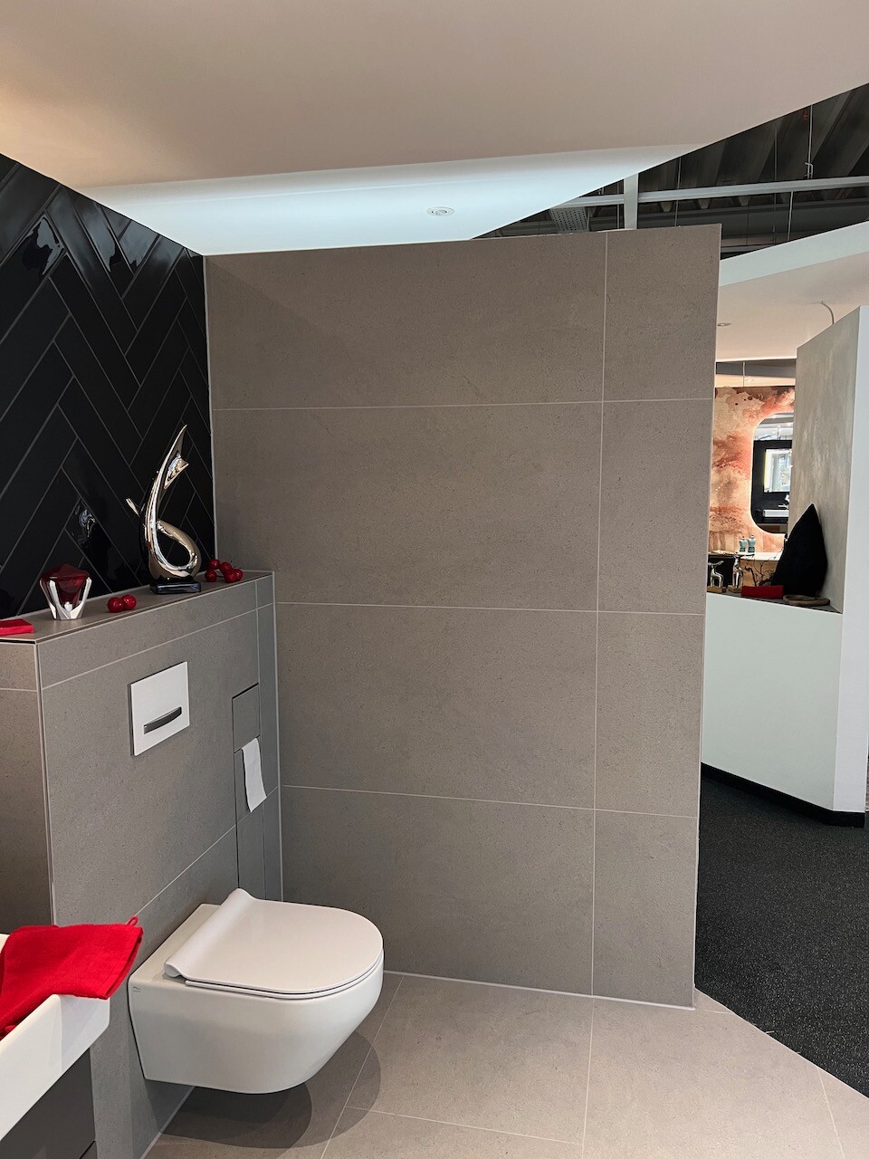 Modernes Badezimmer mit wandhängendem WC, grauen Fliesen und roter Deko auf dem Spülkasten.