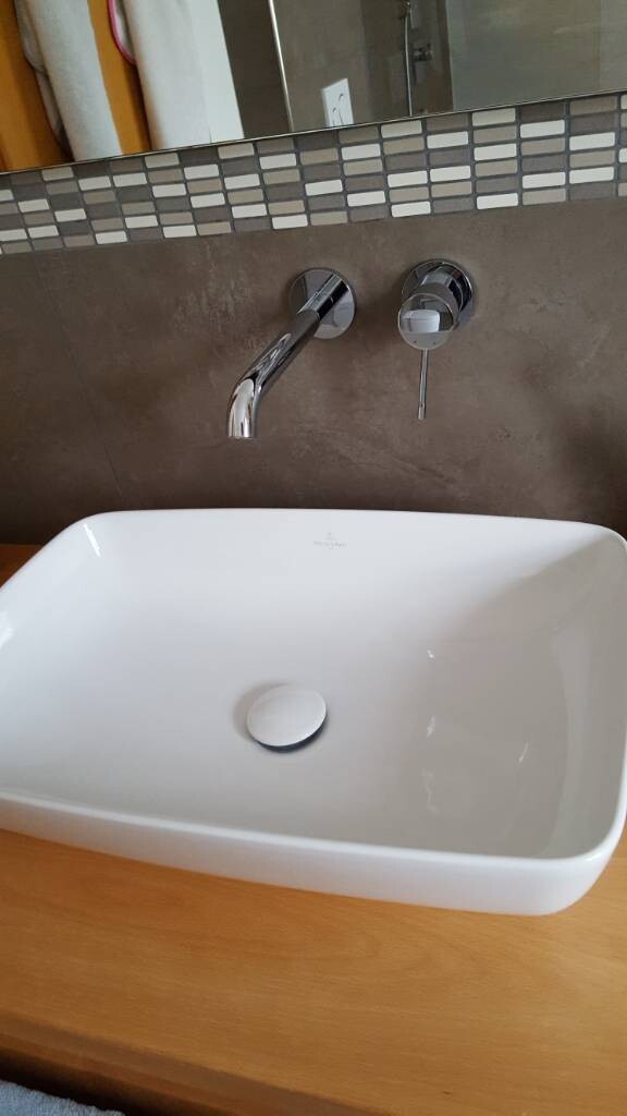 Modernes Badezimmer-Waschtisch mit Wandarmatur vor grauer Fliesenrückwand.