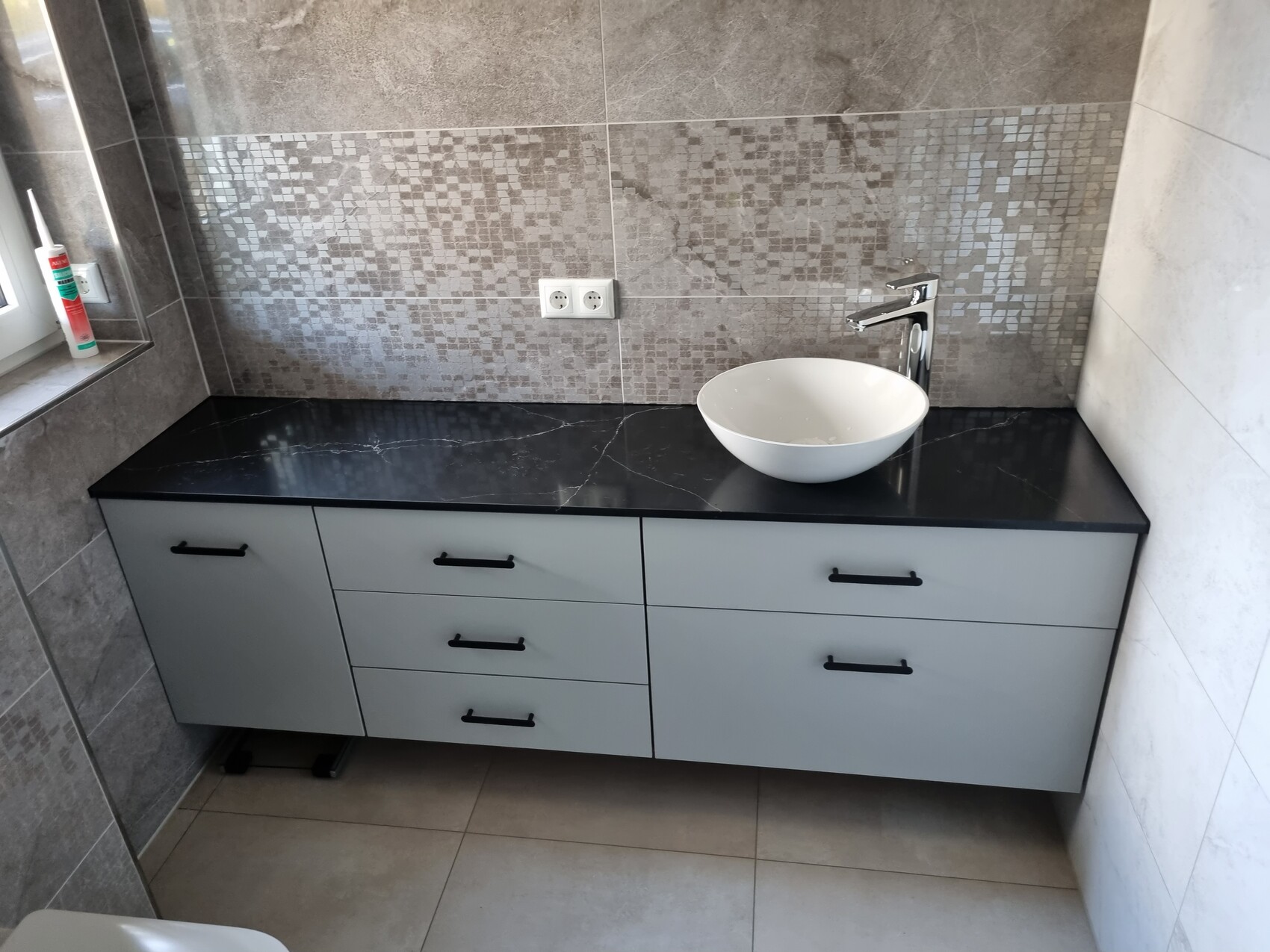 Moderne Badezimmer-Waschtisch mit schwarzer Platte, runde weiße Spüle, Mosaik-Rückwand, Chromarmatur.