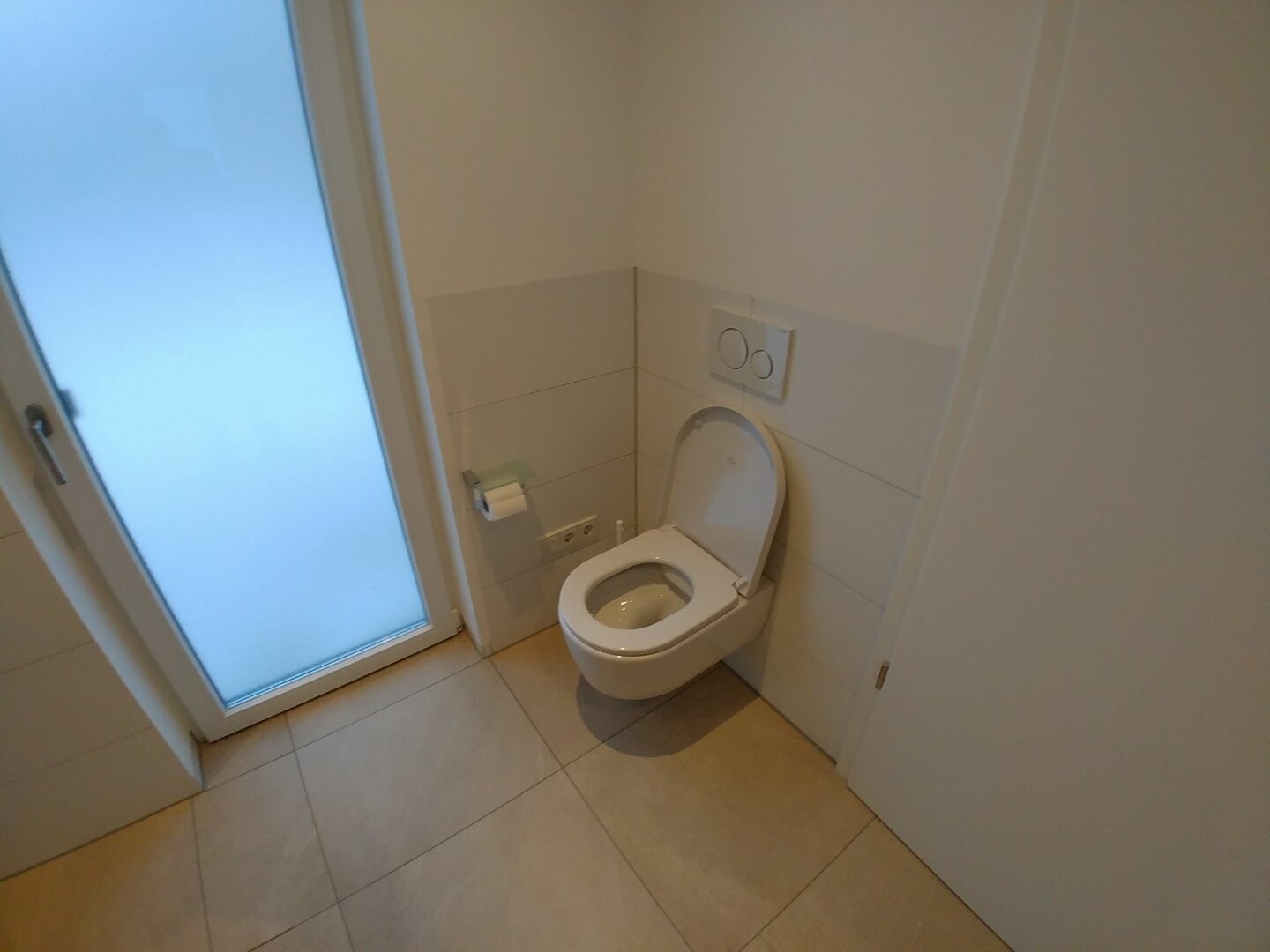 Modernes WC mit Wand-Spülkasten, Sitz hoch, Papierhalter daneben, Glastür links