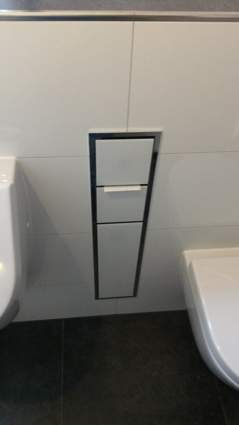 Modernes Badezimmer mit Spülkasten hinter vertikalem Metallrahmen an Wandfliesen; Toilette links.