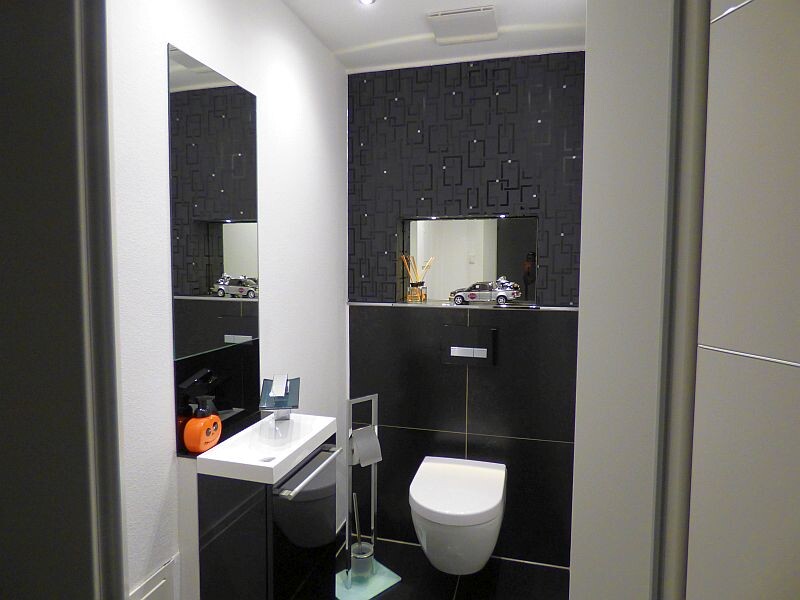 Modernes Badezimmer mit weißem Waschbecken, Spiegel, schwarzer Fliesenwand und wandhängendem WC.