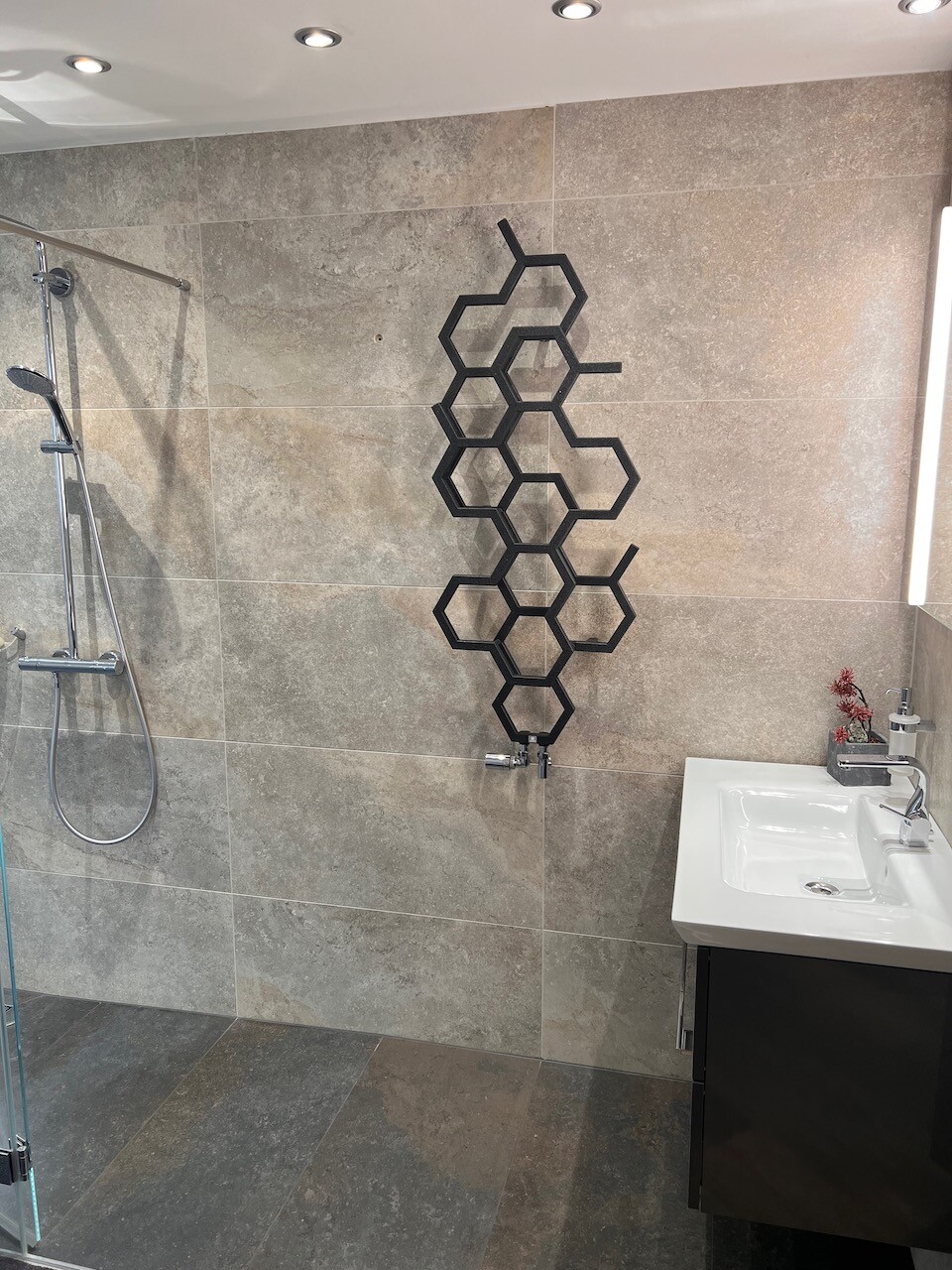 Modernes Badezimmer mit grauen Fliesen, Dusche links, schwarze Hexagon-Wanddekoration.