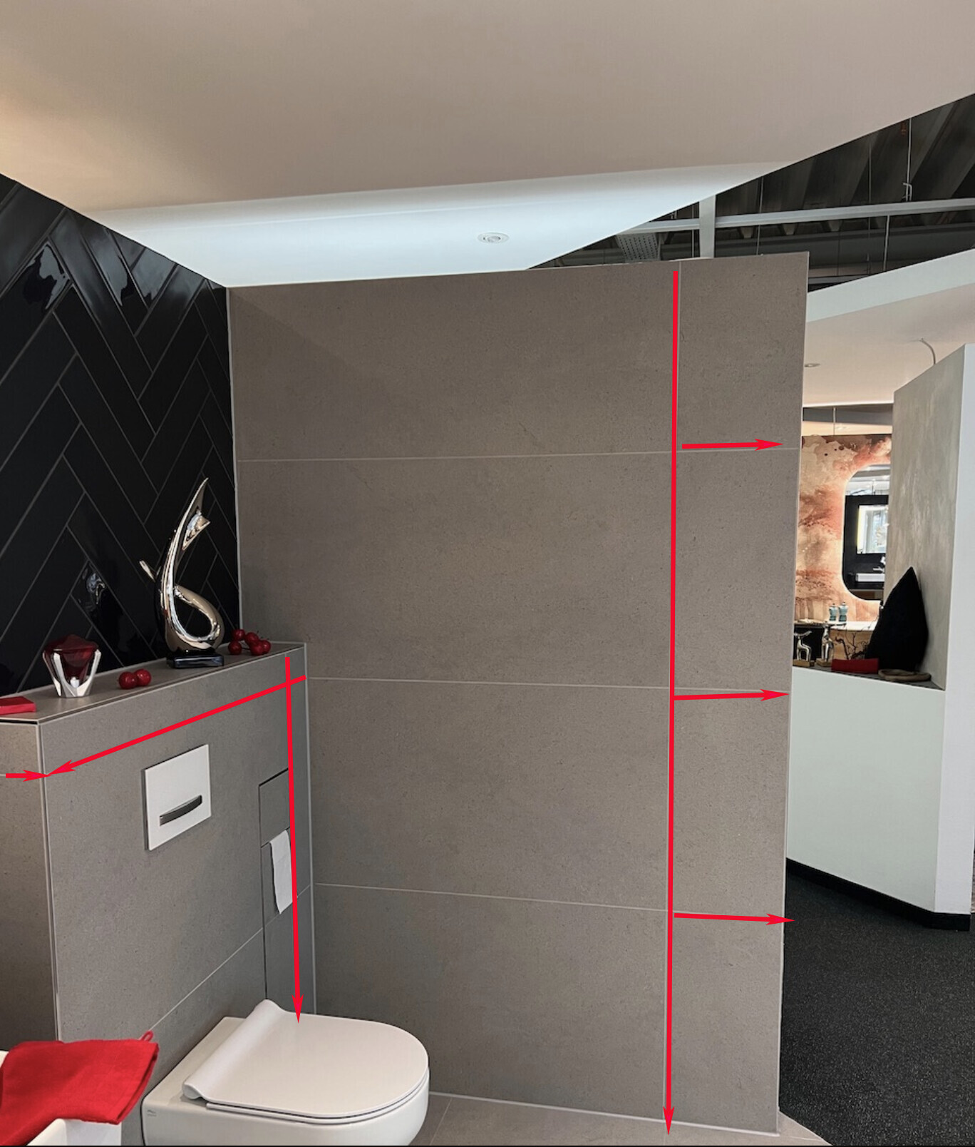 Moderne Badezimmerausstellung mit grauen Fliesen, Toilette, rotem Handtuch und roten Messlinien.