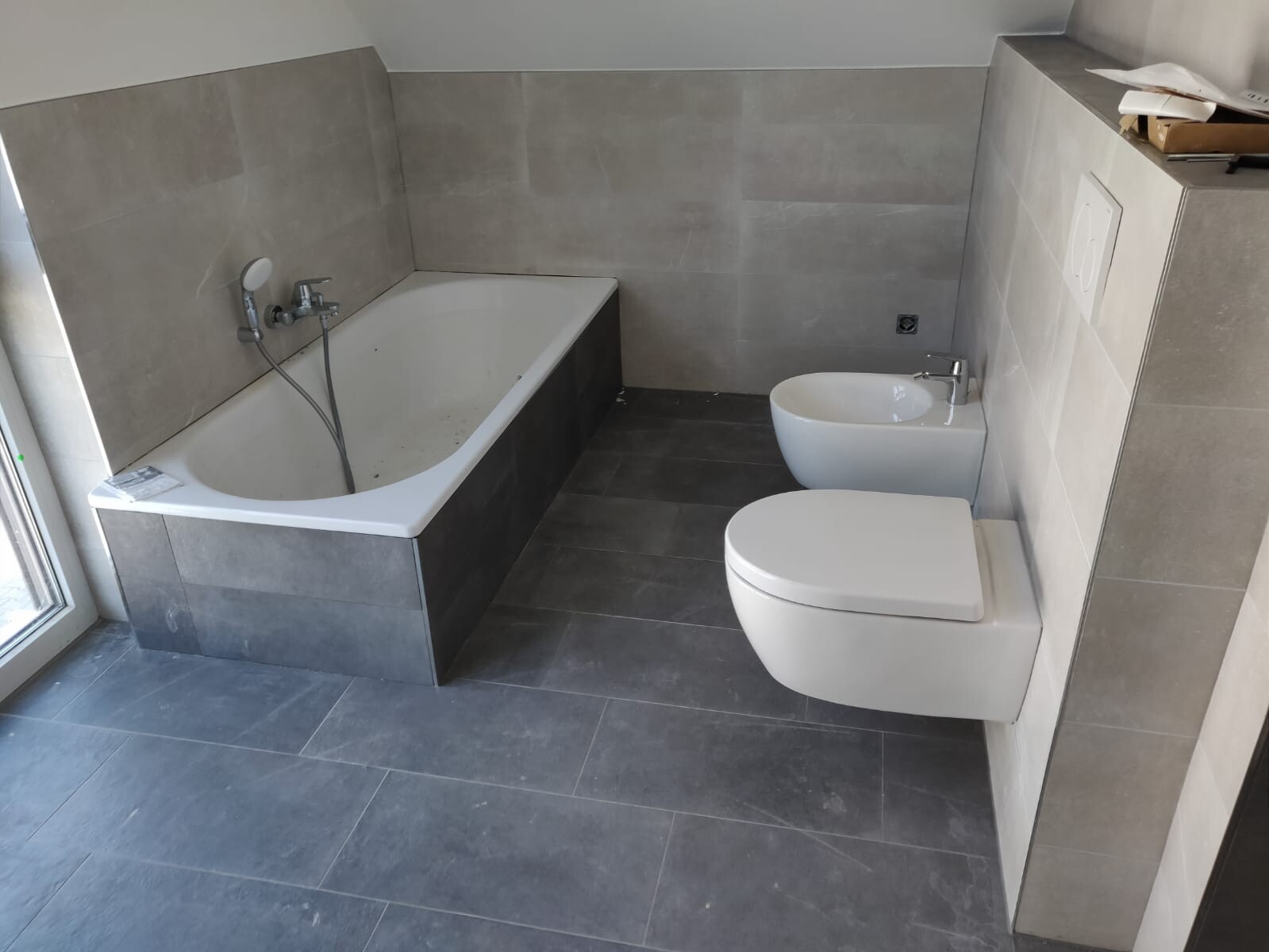 moderner-badraum-mit-wanne-und-toilette-grau-fliesen.jpeg