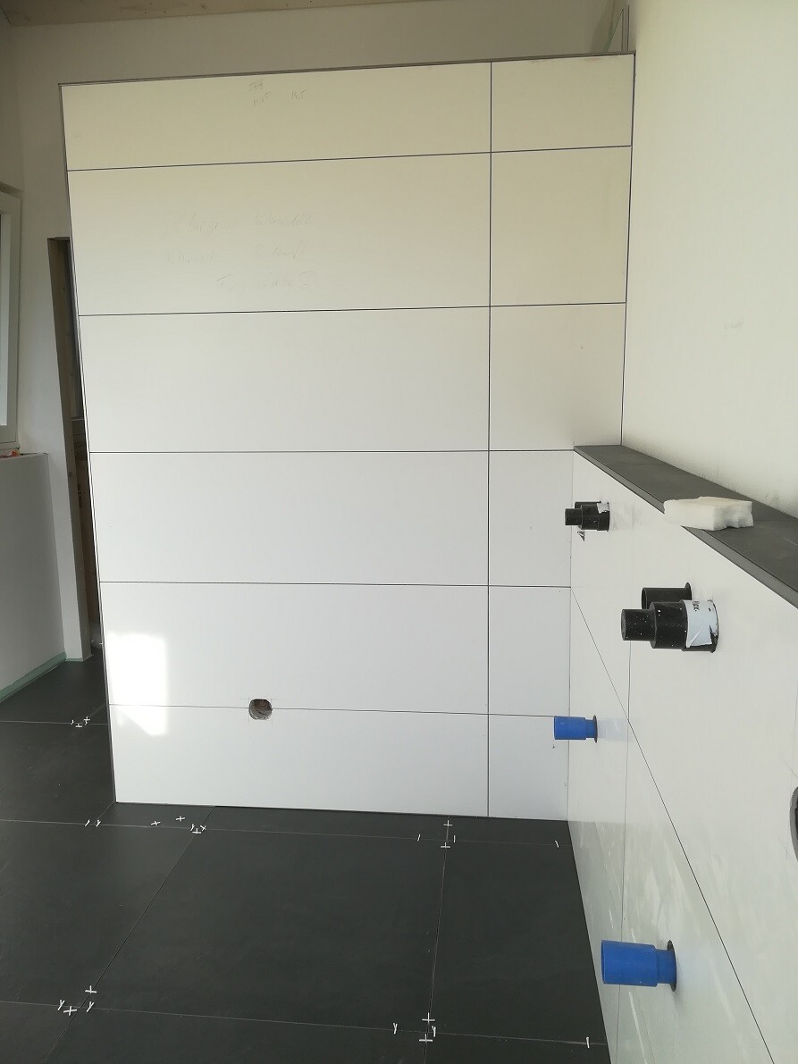 Weiße Fliesenwand mit Fugen; blaue Rohre ragen aus der Wand, dunkler Boden.
