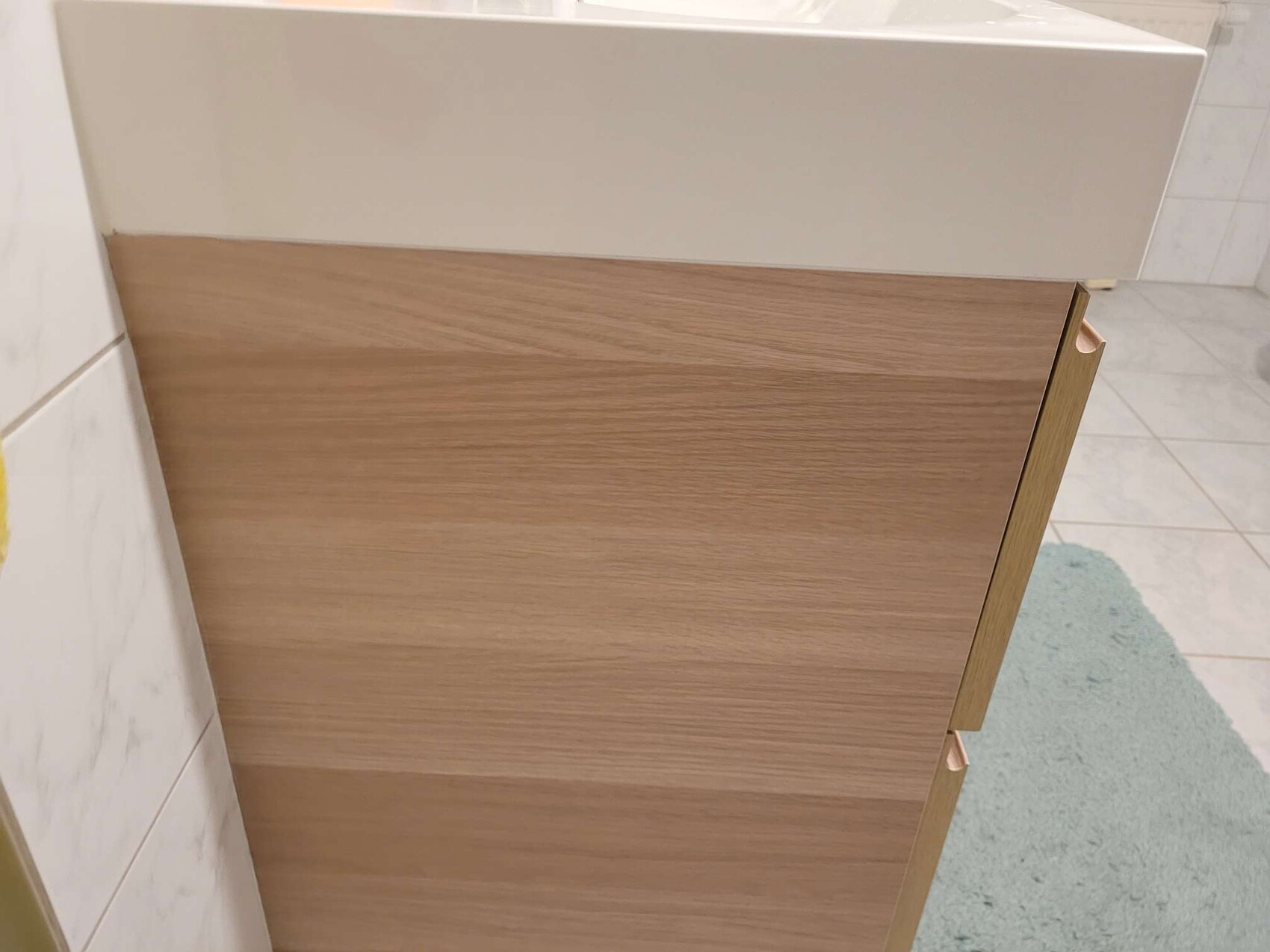 Moderner Badunterschrank aus Holzoptik mit weißer Waschtischplatte im Badezimmer.